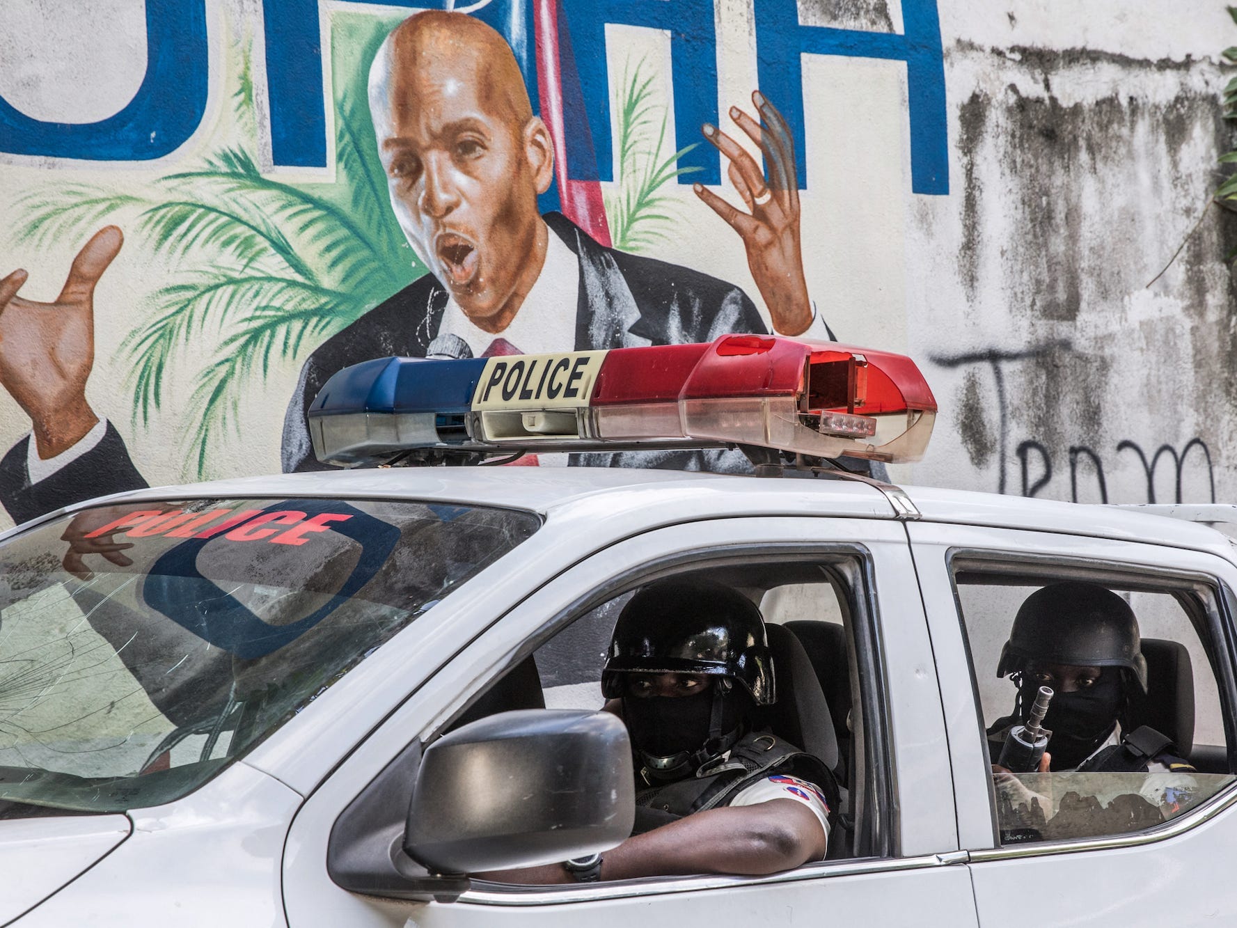 A police convoy drives past a wall painted with the president's image down the alley of the entrance to the residence of the president in Port-au-Prince on July 15, 2021, in the wake of Haitian President Jovenel Moise's assassination on July 7, 2021.