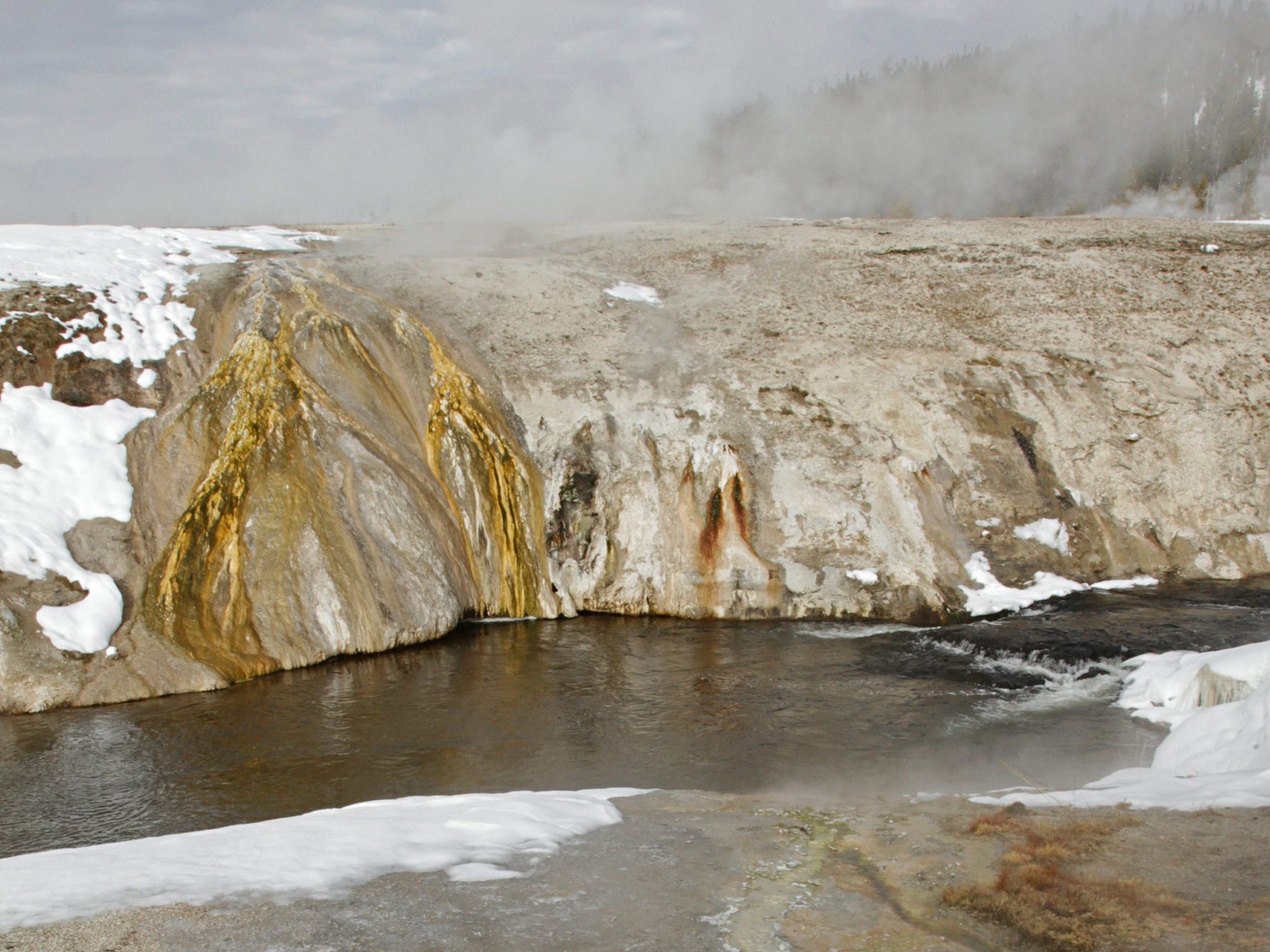 A natural spring with rising steam and surrounded by snow.