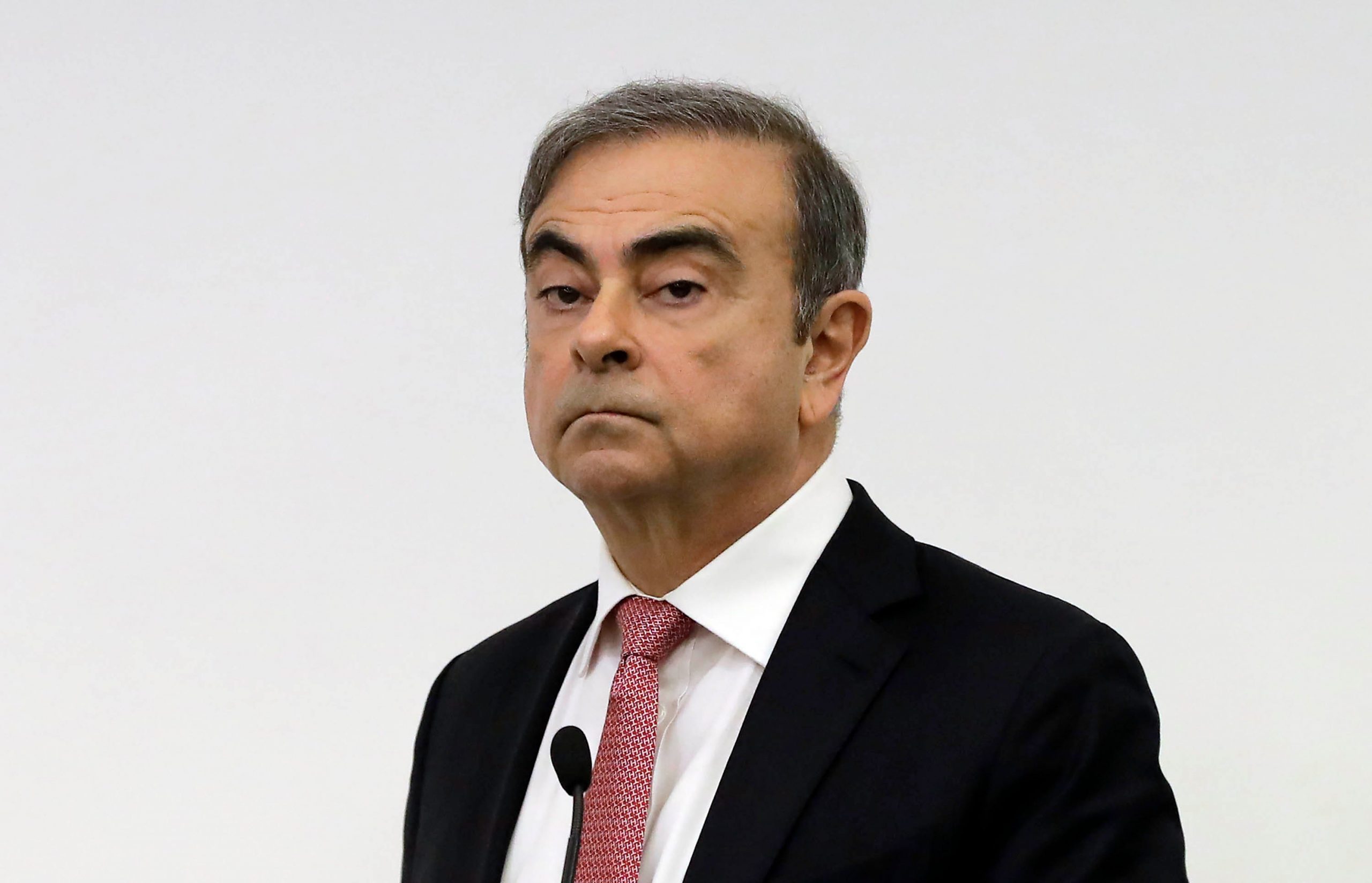 Former Nissan chairman Carlos Ghosn wears a black suit jacket, white shirt and pink tie.