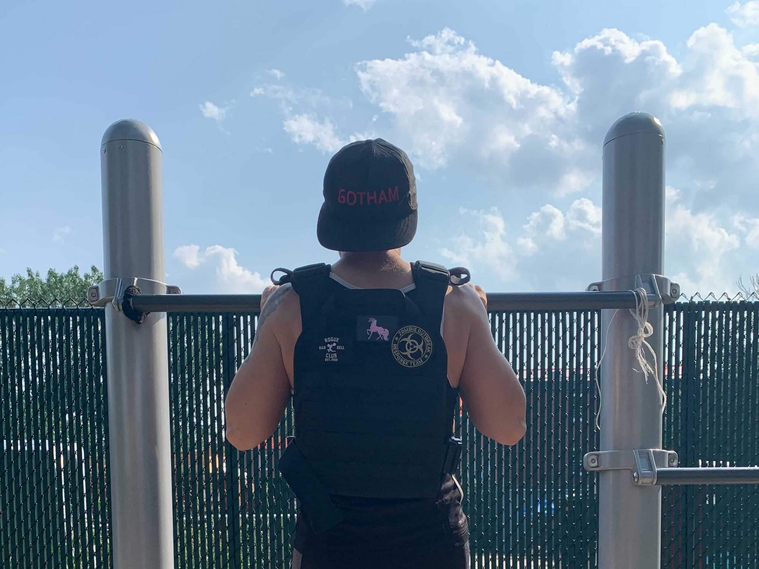 a sweaty fitness reporter at the top of a pull-up on a playground, wearing a weight vest