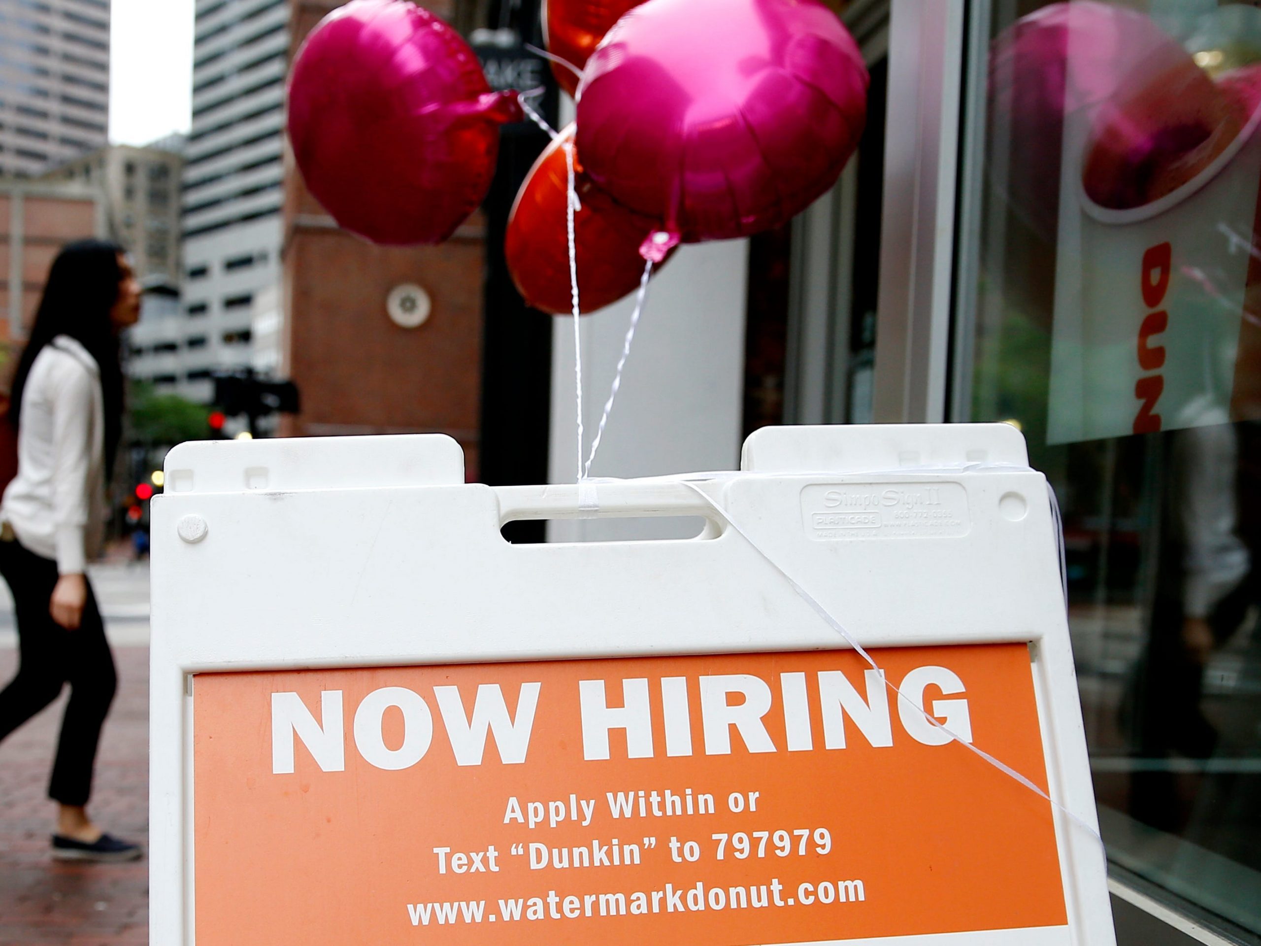 A orange sign with pink balloons reads "now hiring."