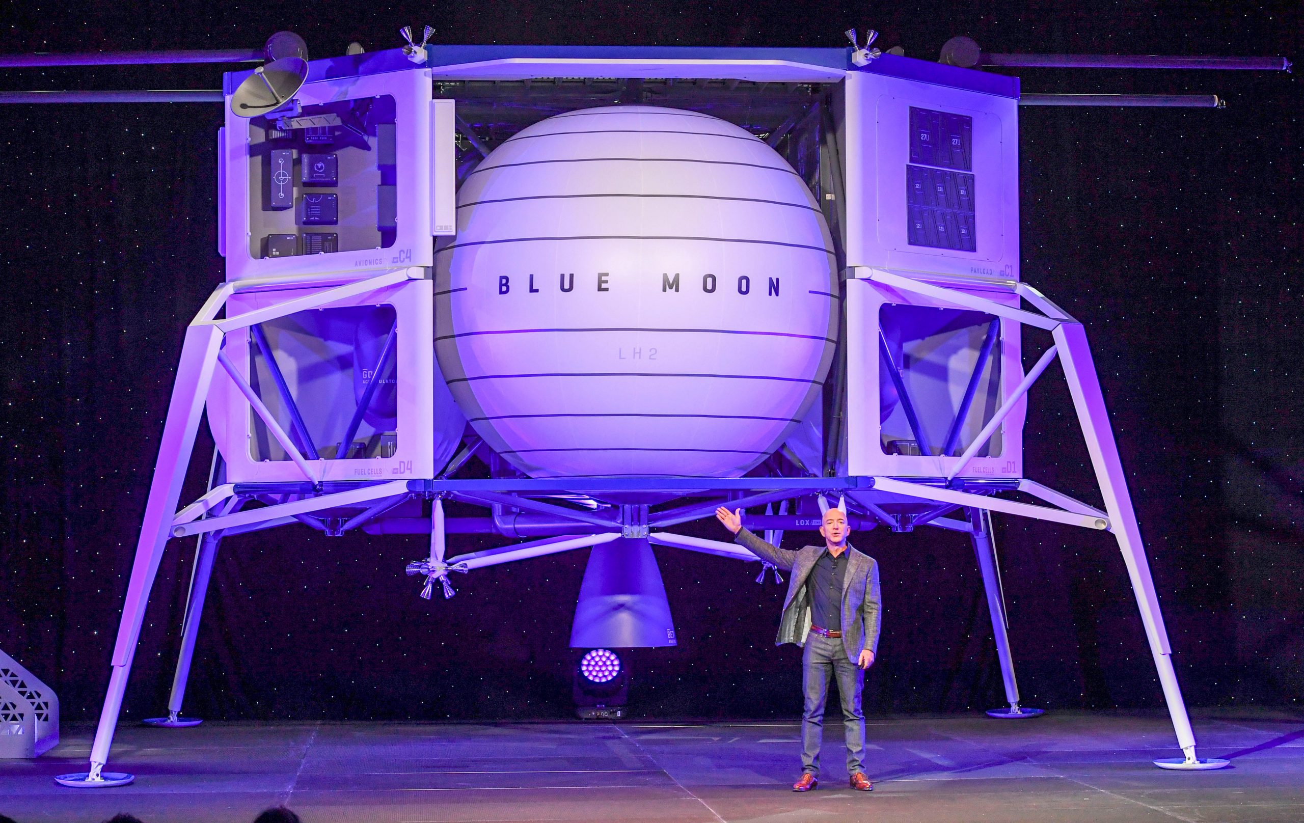 Jeff Bezos gesturing towards a space lander, which looks like an orb with four legs.