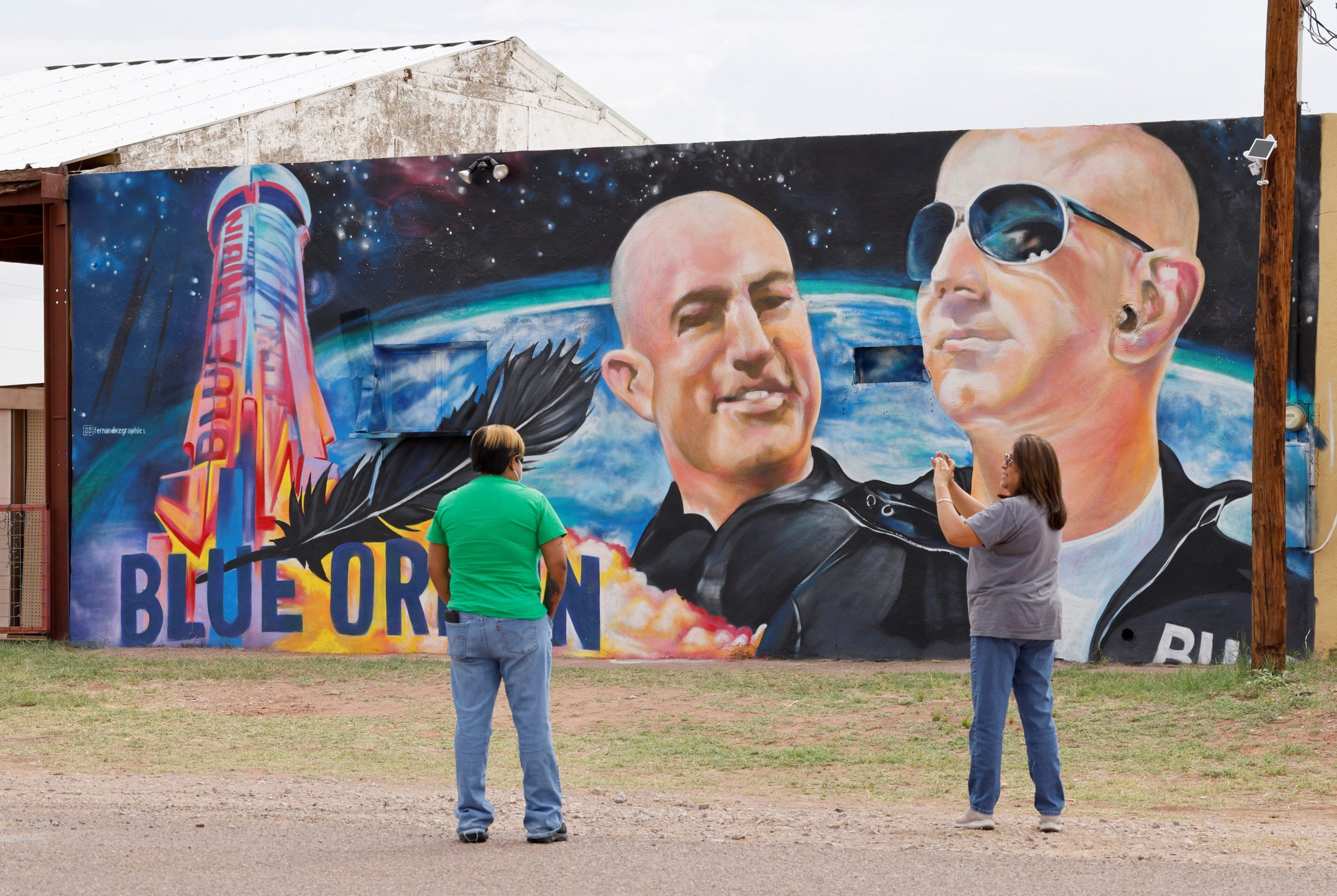 A woman photographs another person in front of a mural showing Jeff Bezos and a space launch.