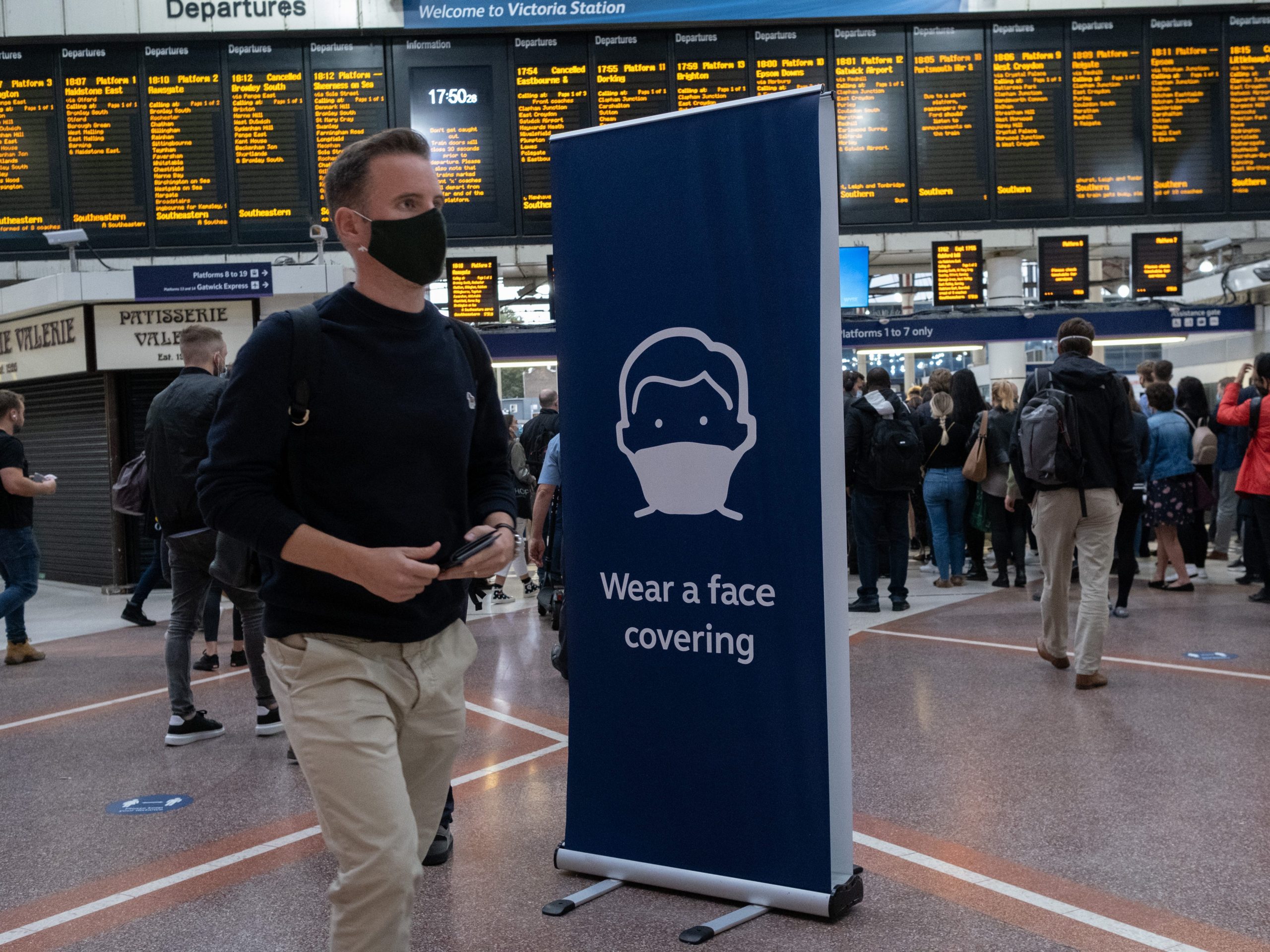 Man wearing a face covering walking through a train station.