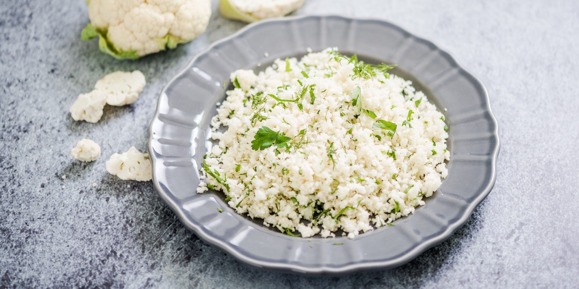 A plate of cauliflower rice studded with herbs surrounded by cauliflower florets