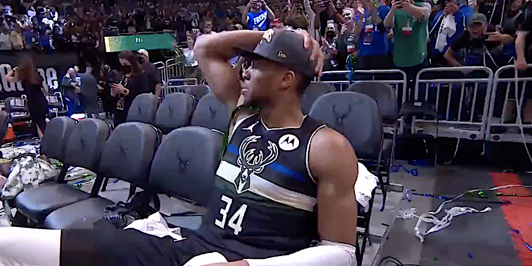 Giannis Antetokounmpo sits on a bench in tears.