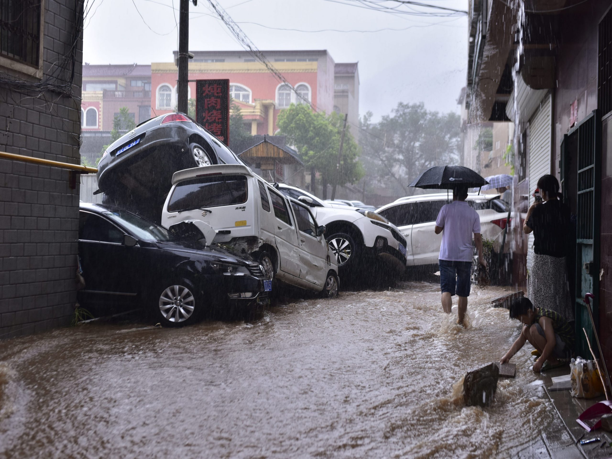 People look at damaged vehicles in a flooded street on July 20, 2021 in Dengfeng, Zhengzhou City, Henan Province of China.