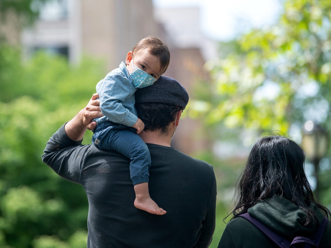 A youngster wearing a mask looks at the camera while sitting on his father's shoulder in Central Park on May 24, 2020 in New York City.