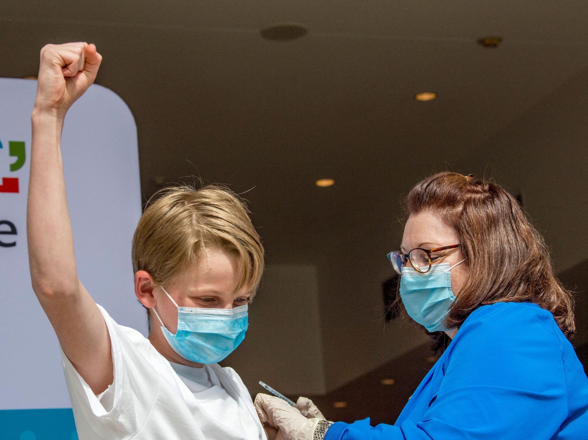 a 13 year old puts his fist in the air, claiming victory after a nurse gave him a COVID-19 shot