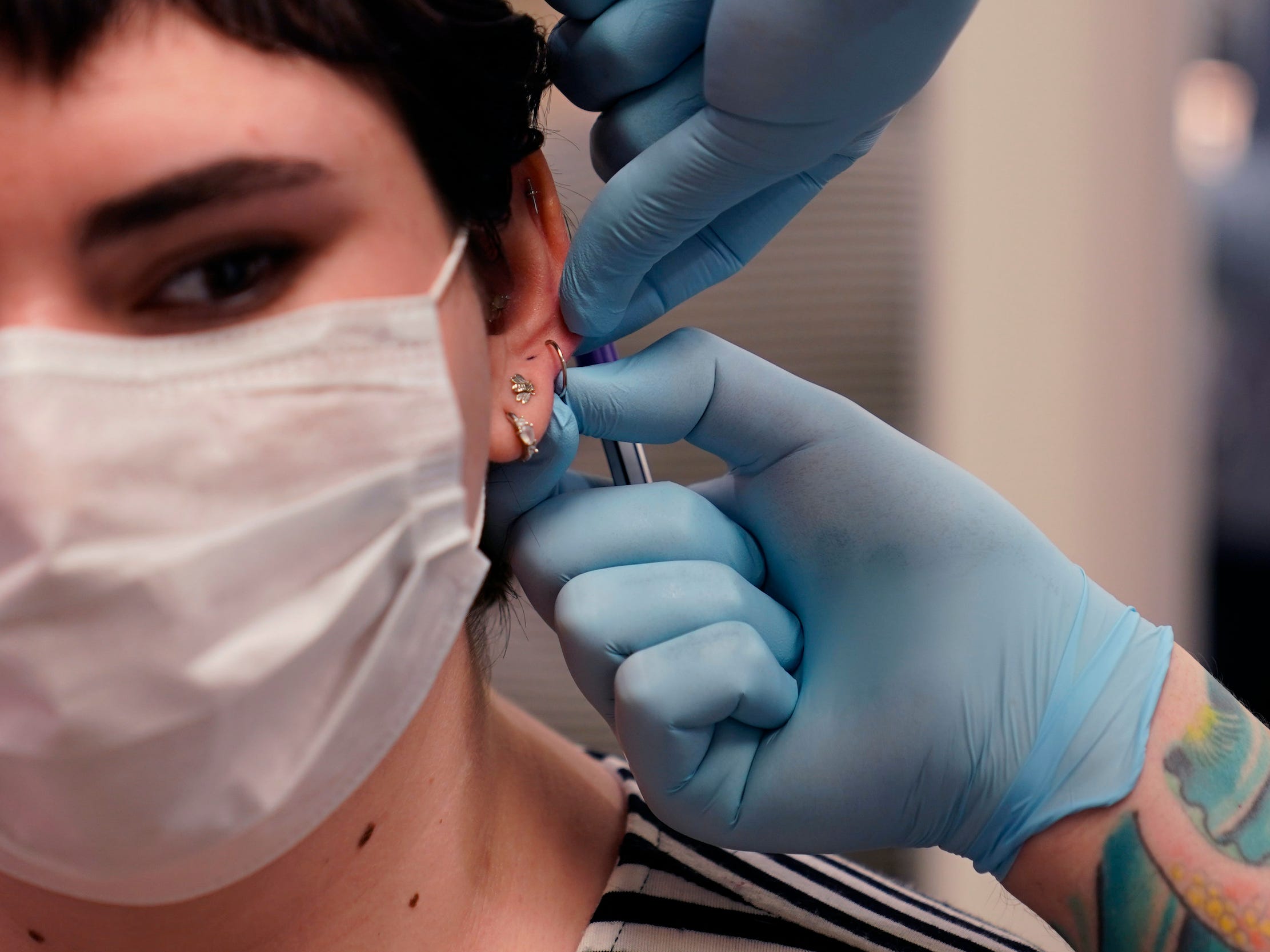 Person wearing gloves holds pierced ear of woman wearing mask