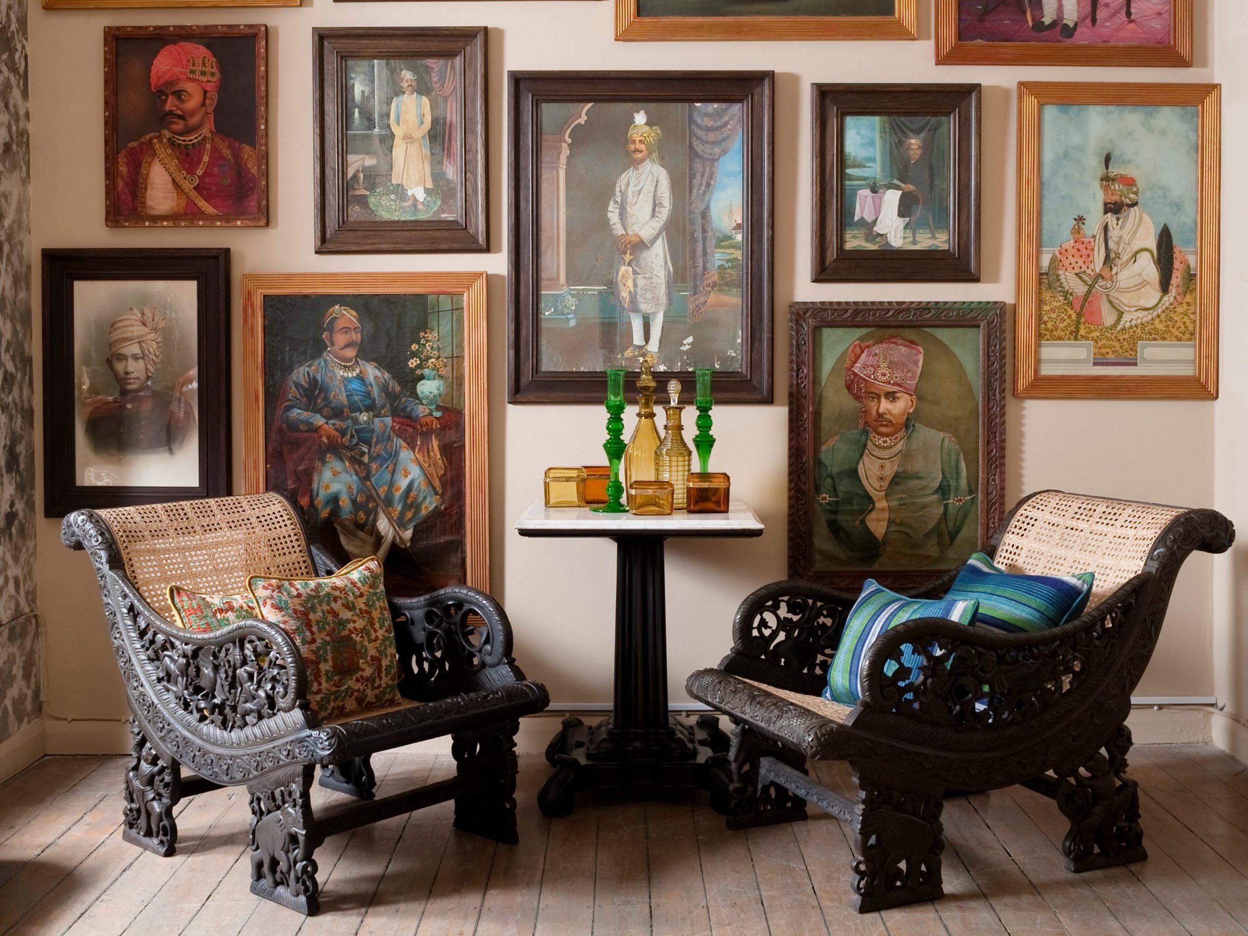 A collection of paintings hang on the wall behind two ornate wooden chairs