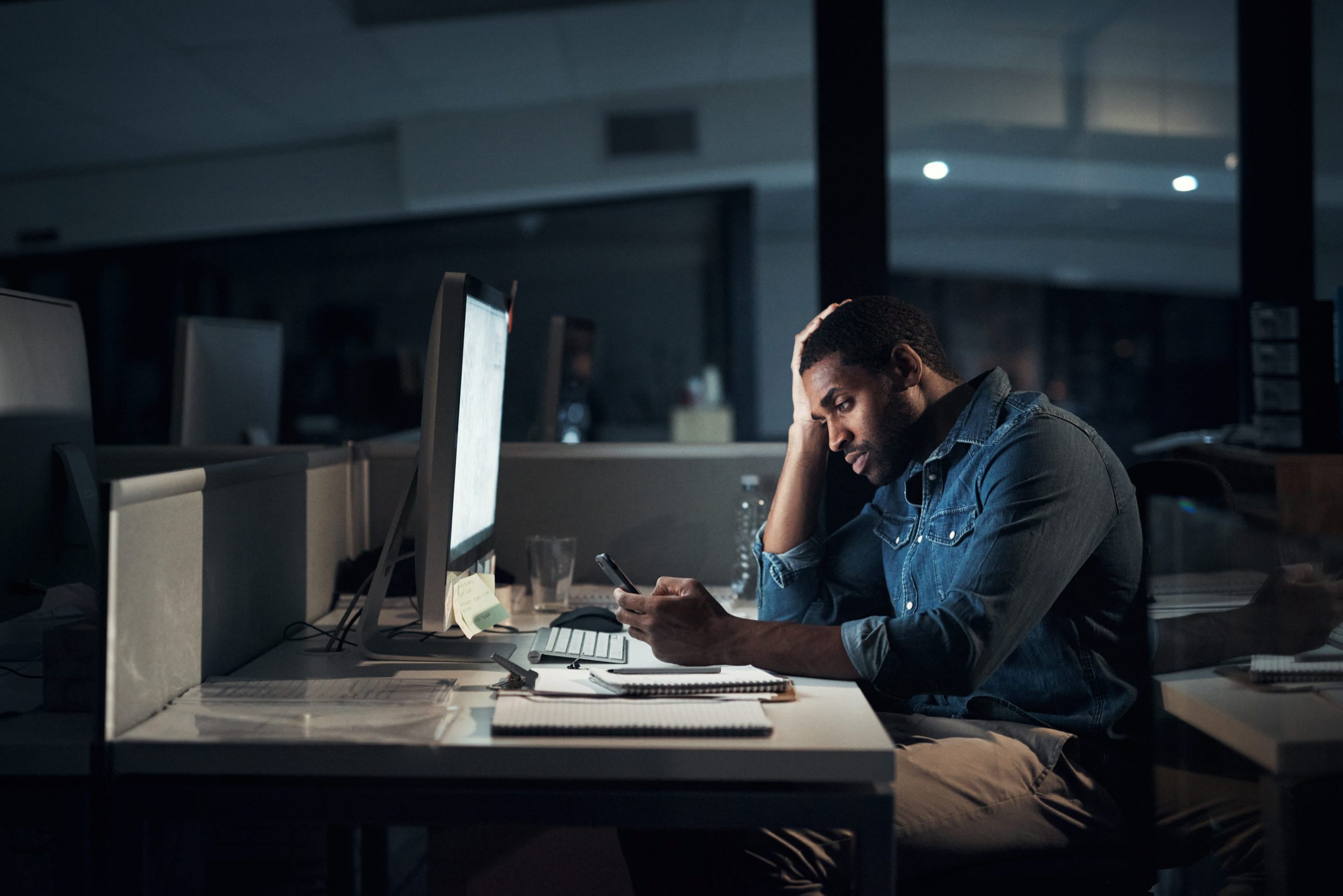 Shot of a young businessman looking stressed while using a smartphone during a late night in a modern office