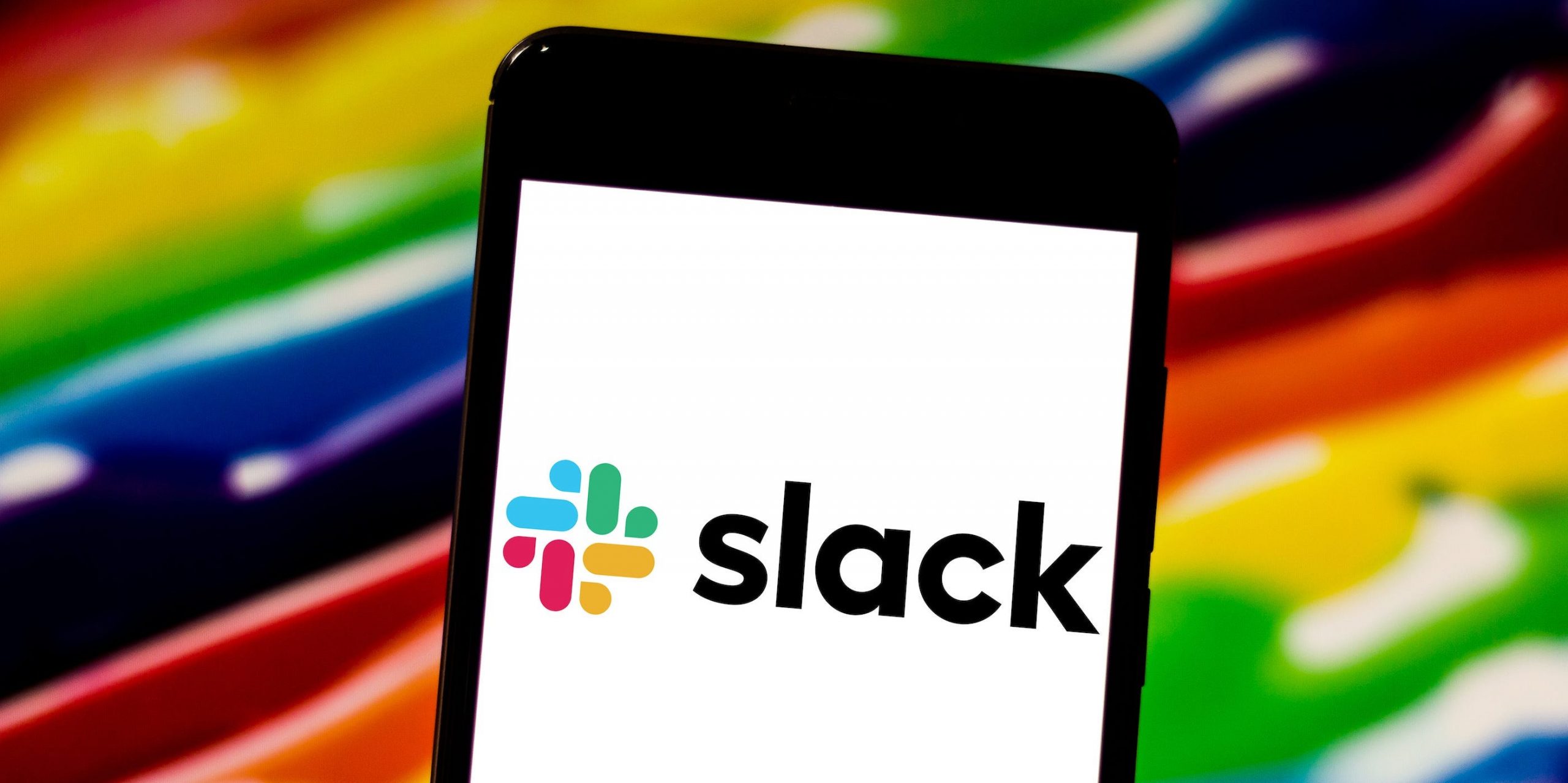 The Slack logo displayed on a phone, in front of a colorful background.