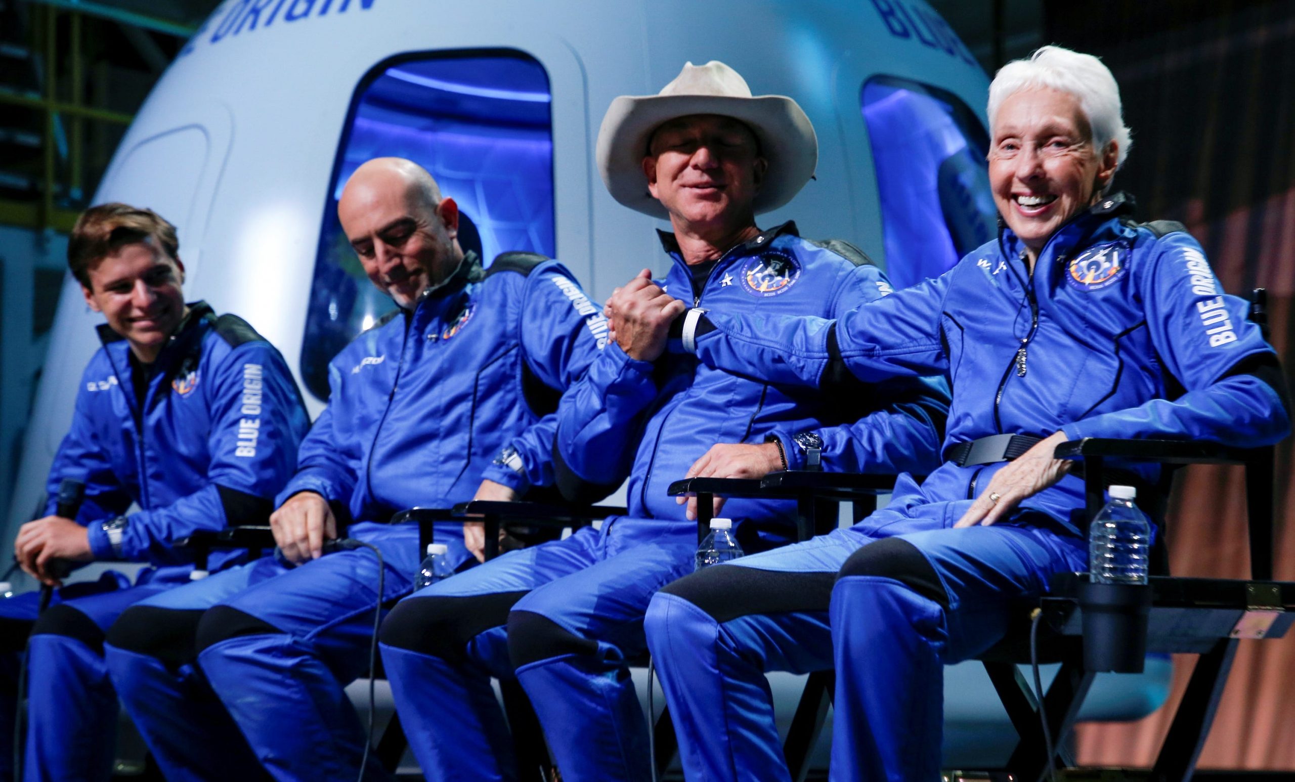 jeff bezos wally funk shake hands sitting on stage in flight suits