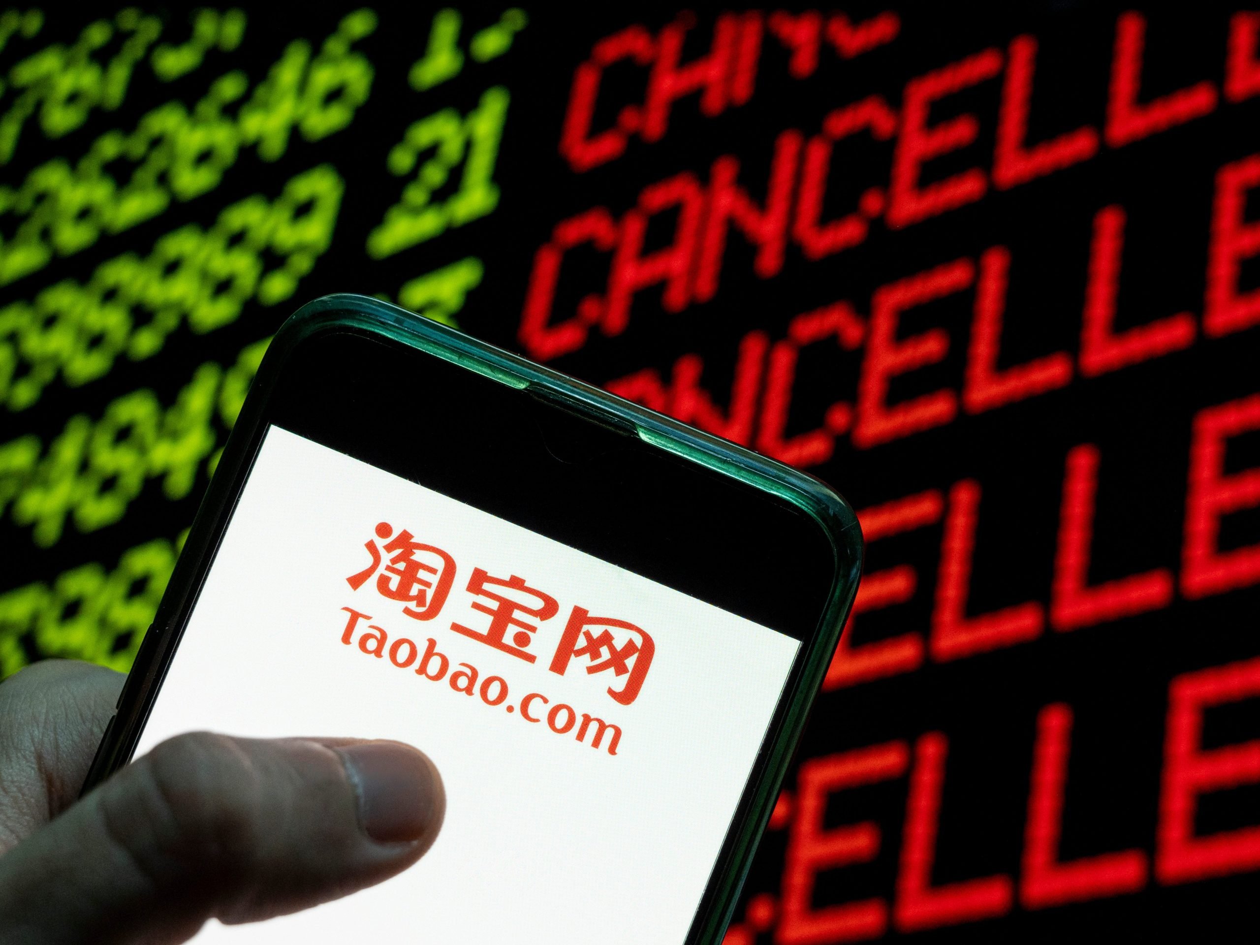 In this photo illustration the Chinese online shopping website owned by Alibaba Group, Taobao logo seen displayed on a smartphone with the word cancelled on a computer screen.