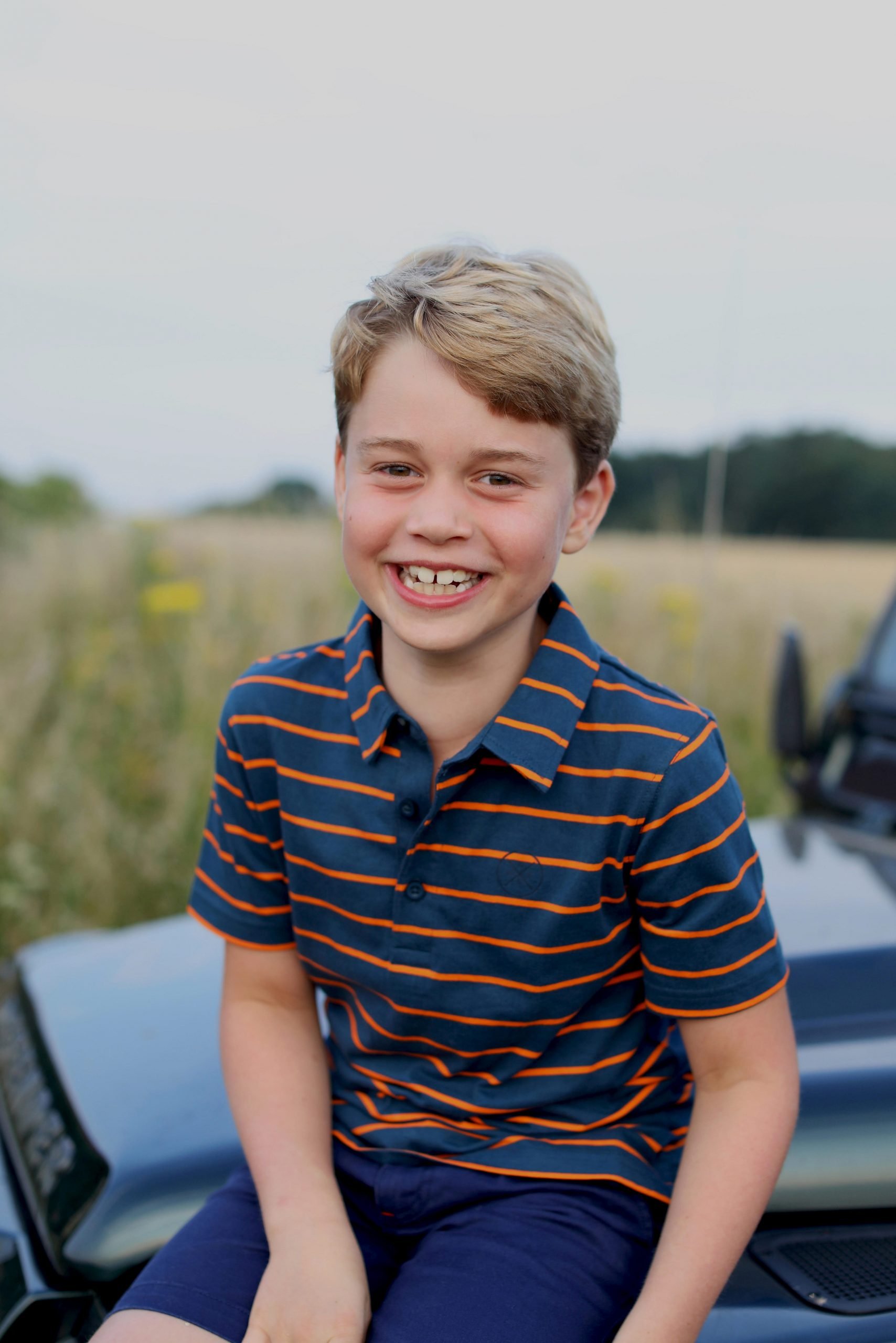 Prince George, who just turned eight, is pictured sitting on the bonnet of a Land Rover Defender wearing a striped polo.