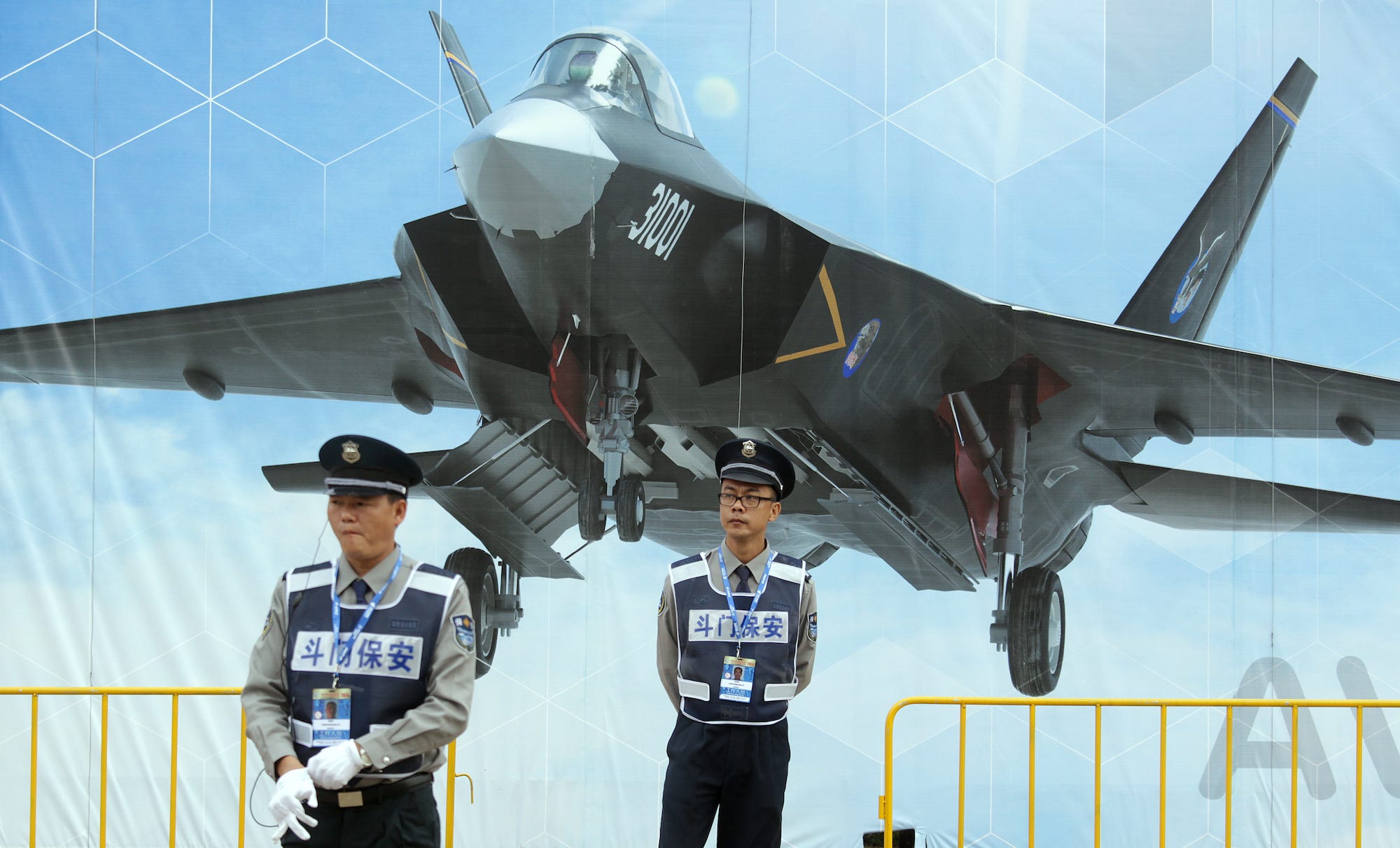 Security guards in front of poster of FC-31 J-31 J-35 fighter jet