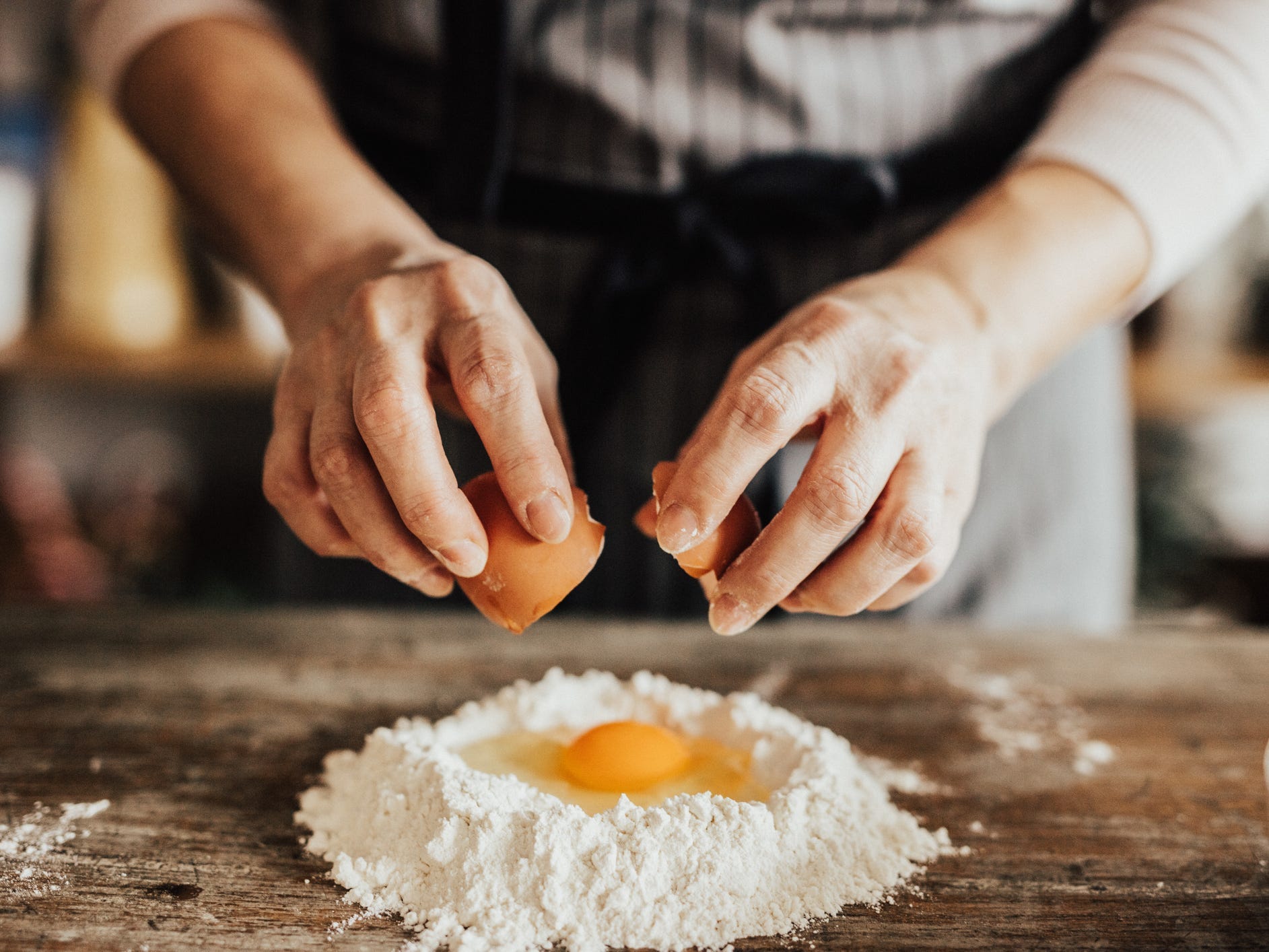 A pair of hands cracks an egg into a pile of flour mounded on a wooden countertop