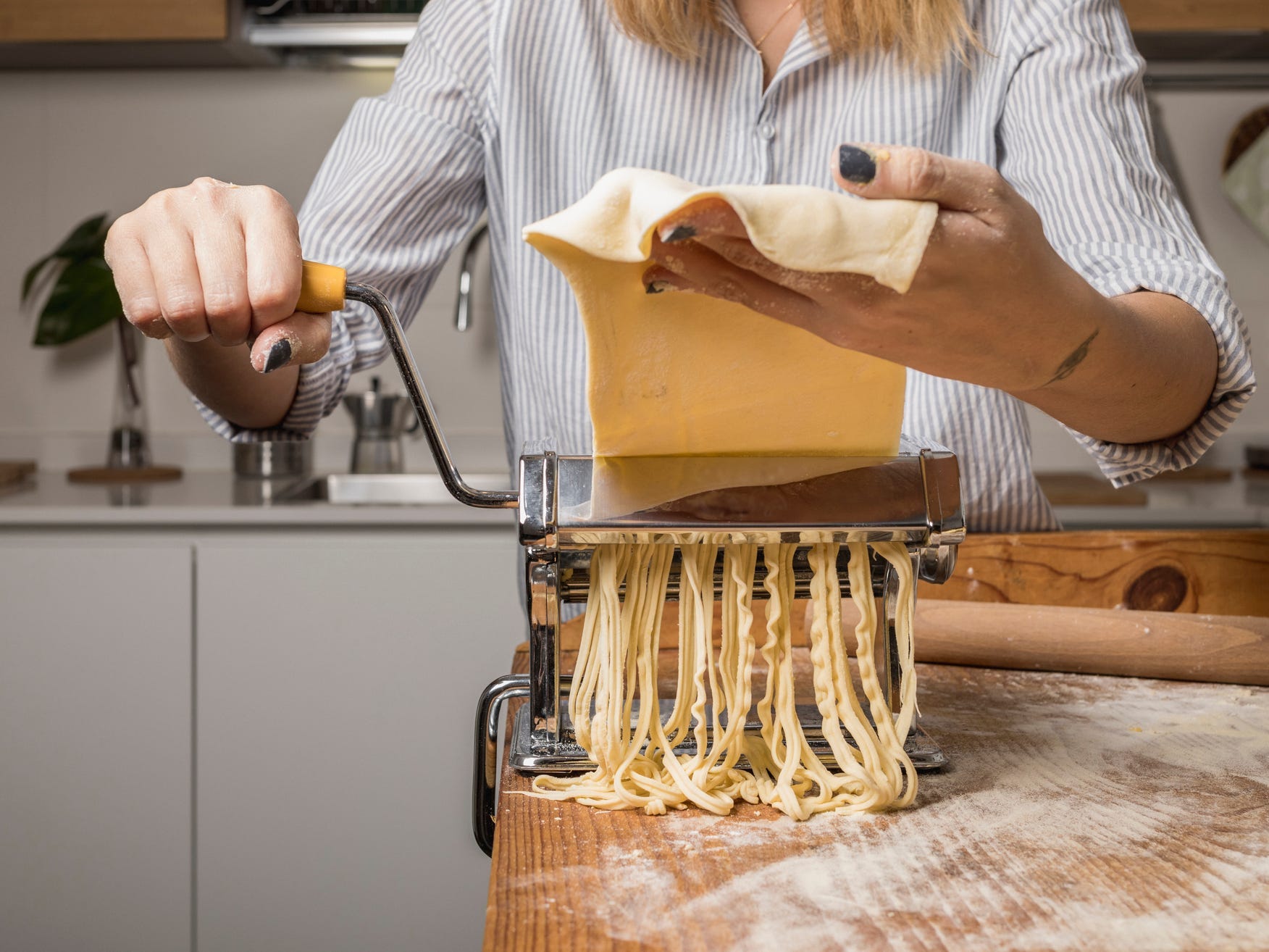 A person runs a sheet of fresh pasta through a tabletop pasta cutter