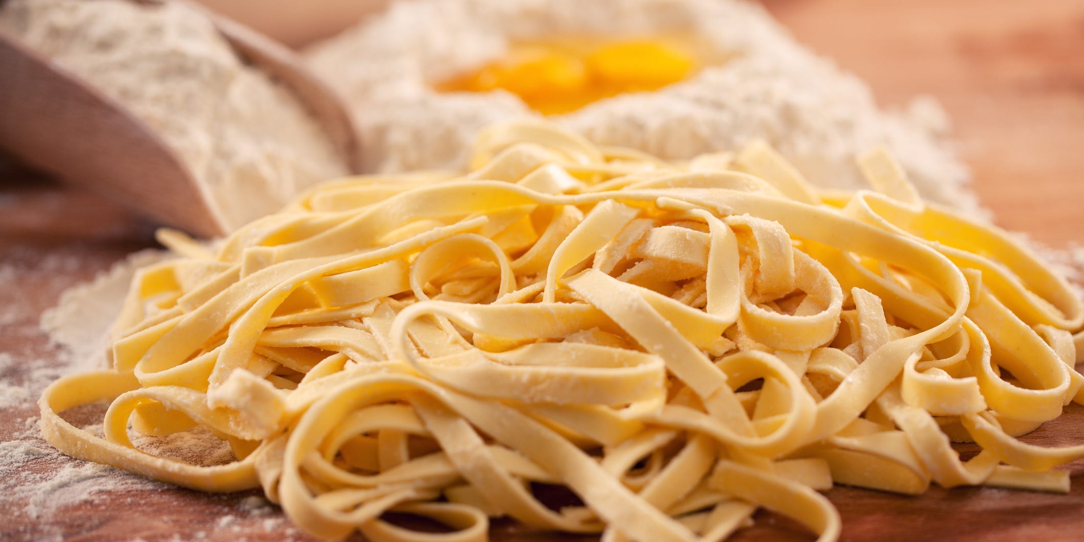 A pile of fresh pasta on a counter in front of a pile of flour with eggs in the middle