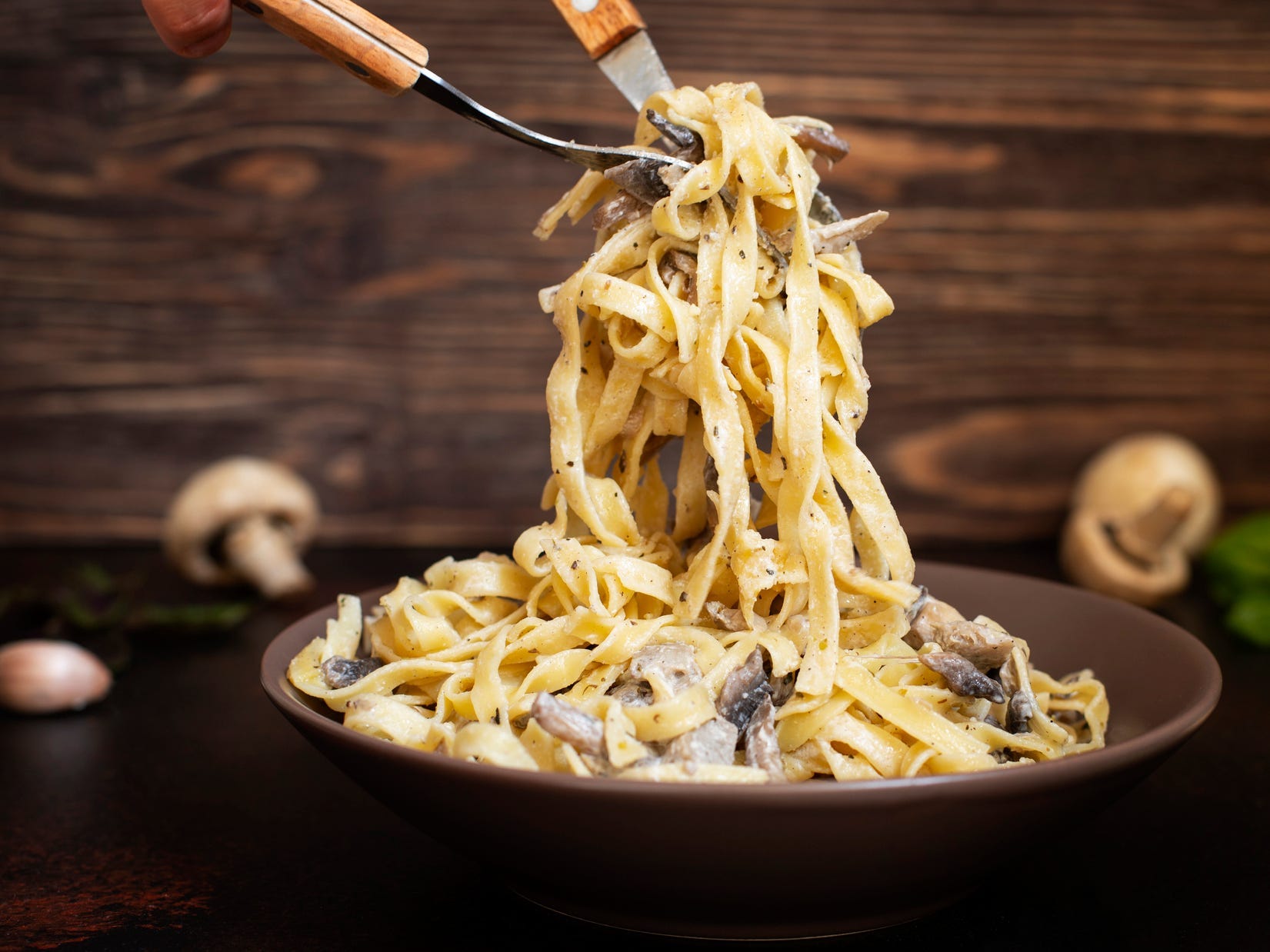 A pair of forks lifting fettuccini out of a bowl