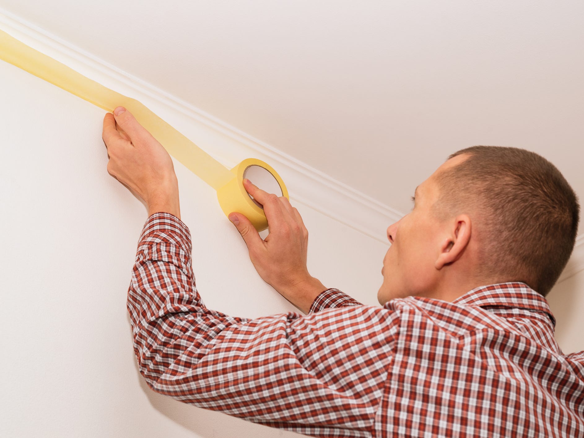 A man applying painter's tape to his ceiling trim