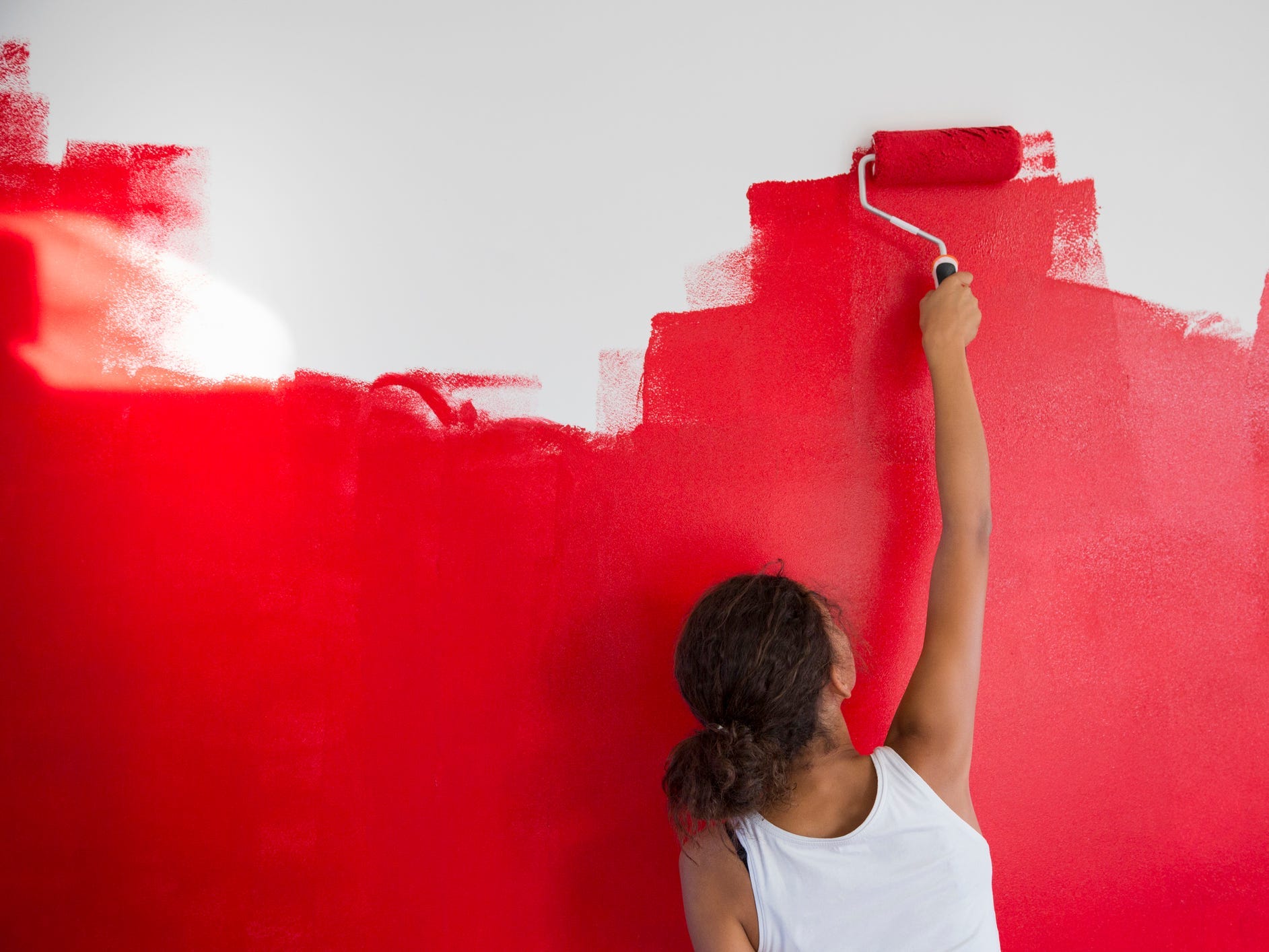 A women painting a wall red with a paint roller