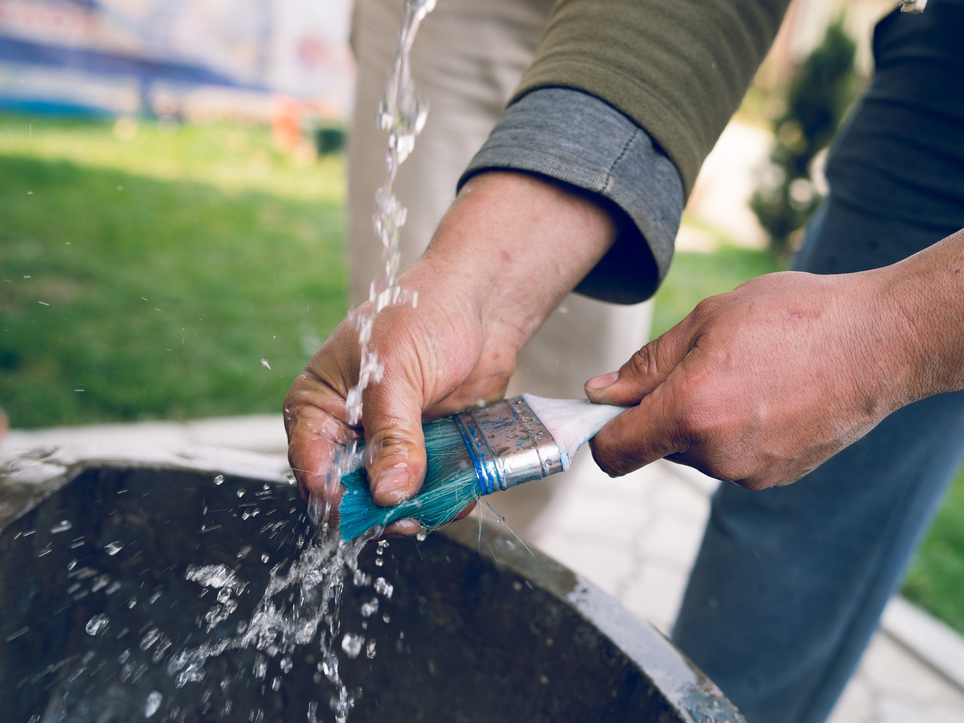 A man washing blue paint off a paintbrush under running water outside