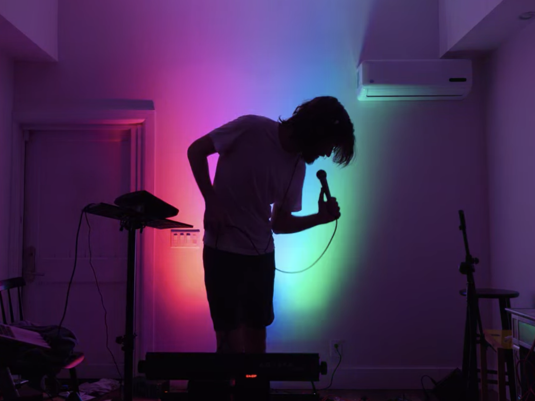 A silhouette of Bo Burnham (a 30-year-old man) singing in front of rainbow lights.
