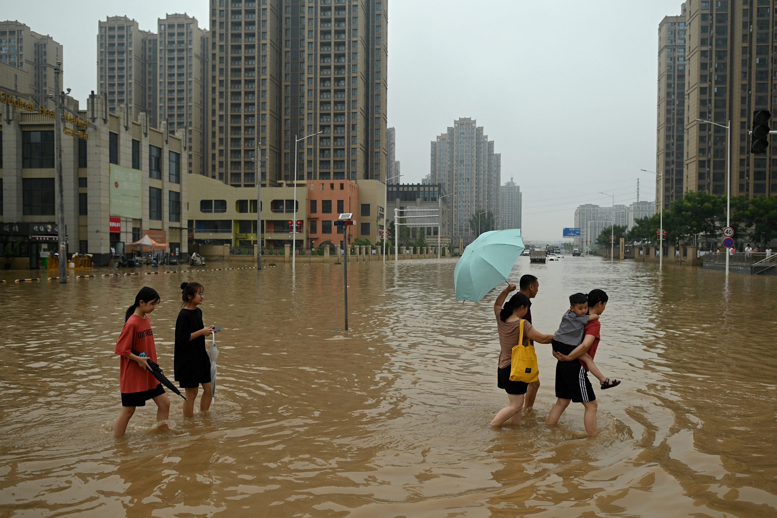 People wade across a flooded street following heavy rains which caused flooding and claimed the lives of at least 33 people earlier in the week, in the city of Zhengzhou in China's Henan province on July 23, 2021.