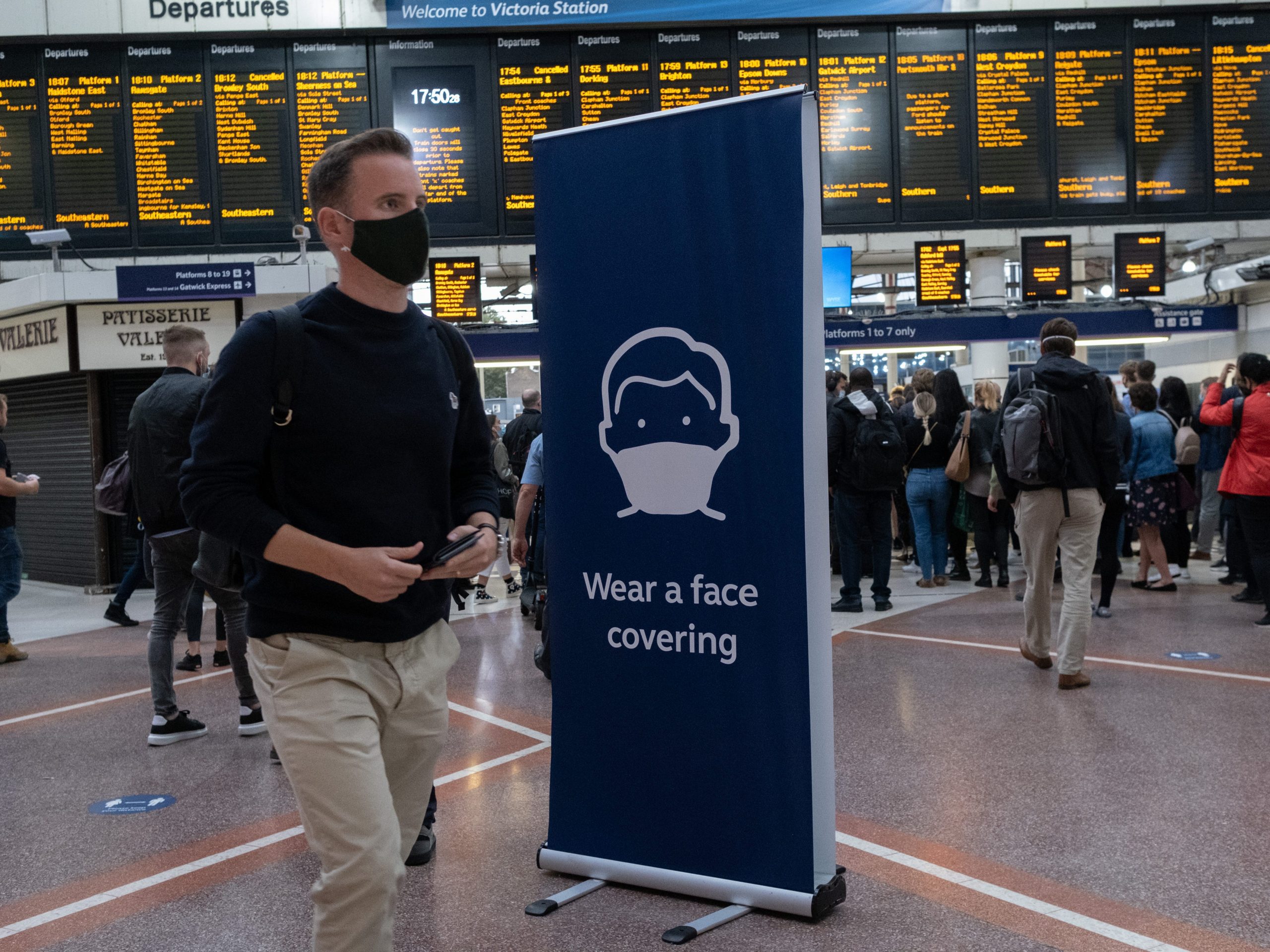 Man wearing a face covering walking through a train station.