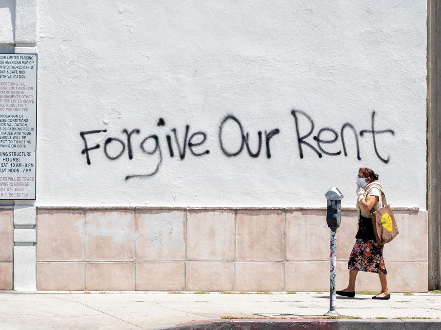 A woman walks past a wall in Los Angeles that has graffiti reading "Forgive Our Rent"