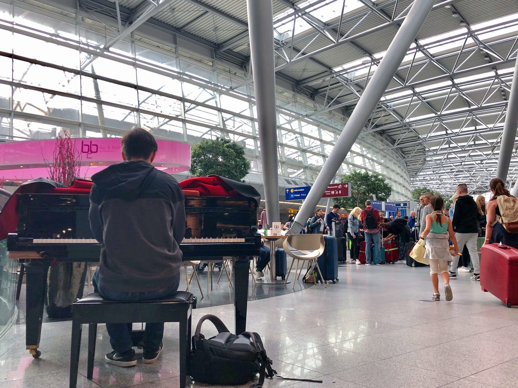 A musician plays the piano at an airport surrounded by travelers walking around a terminal.