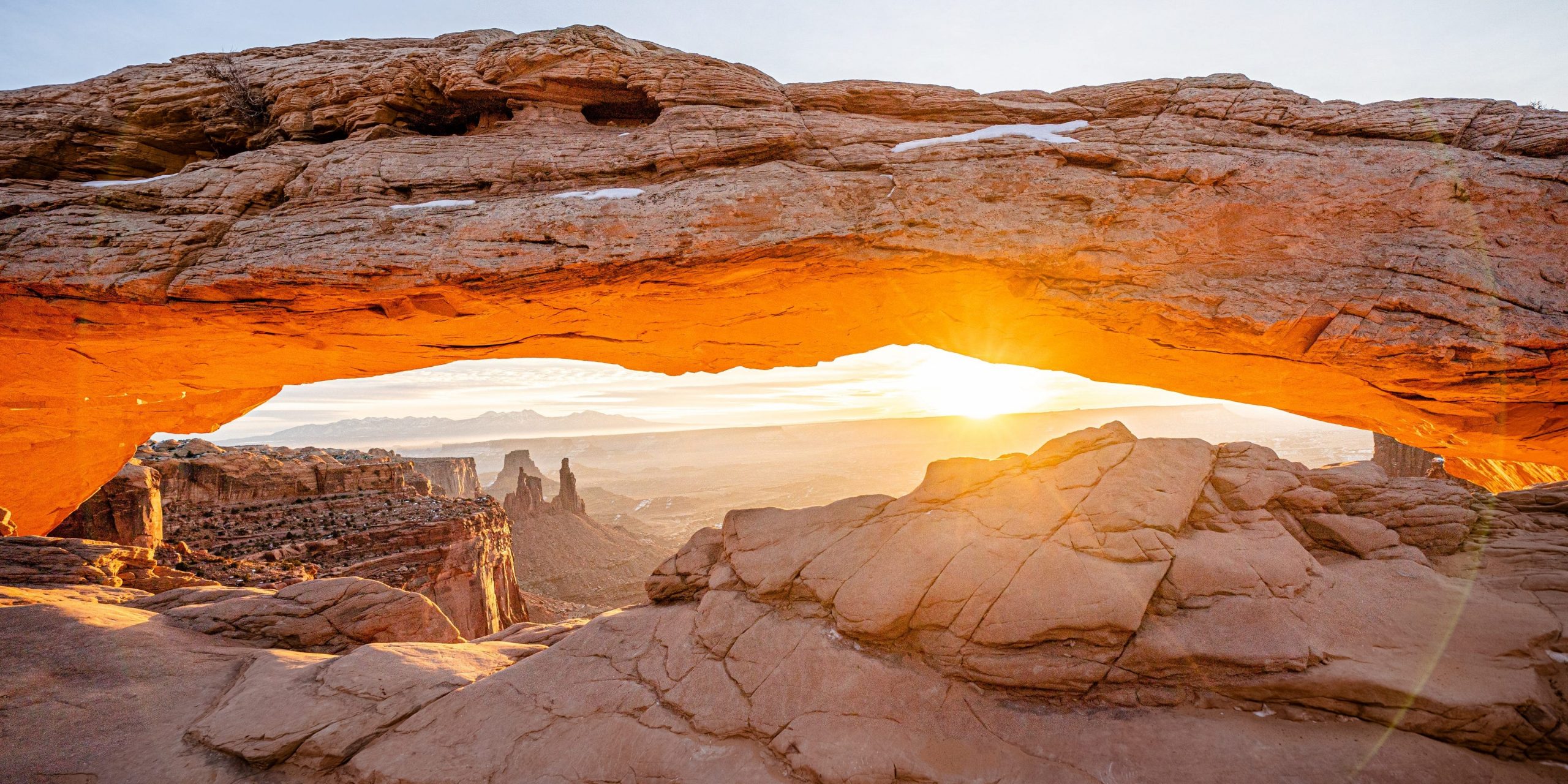 A bright sunrise peaking through the red rock of Mesa Arch.