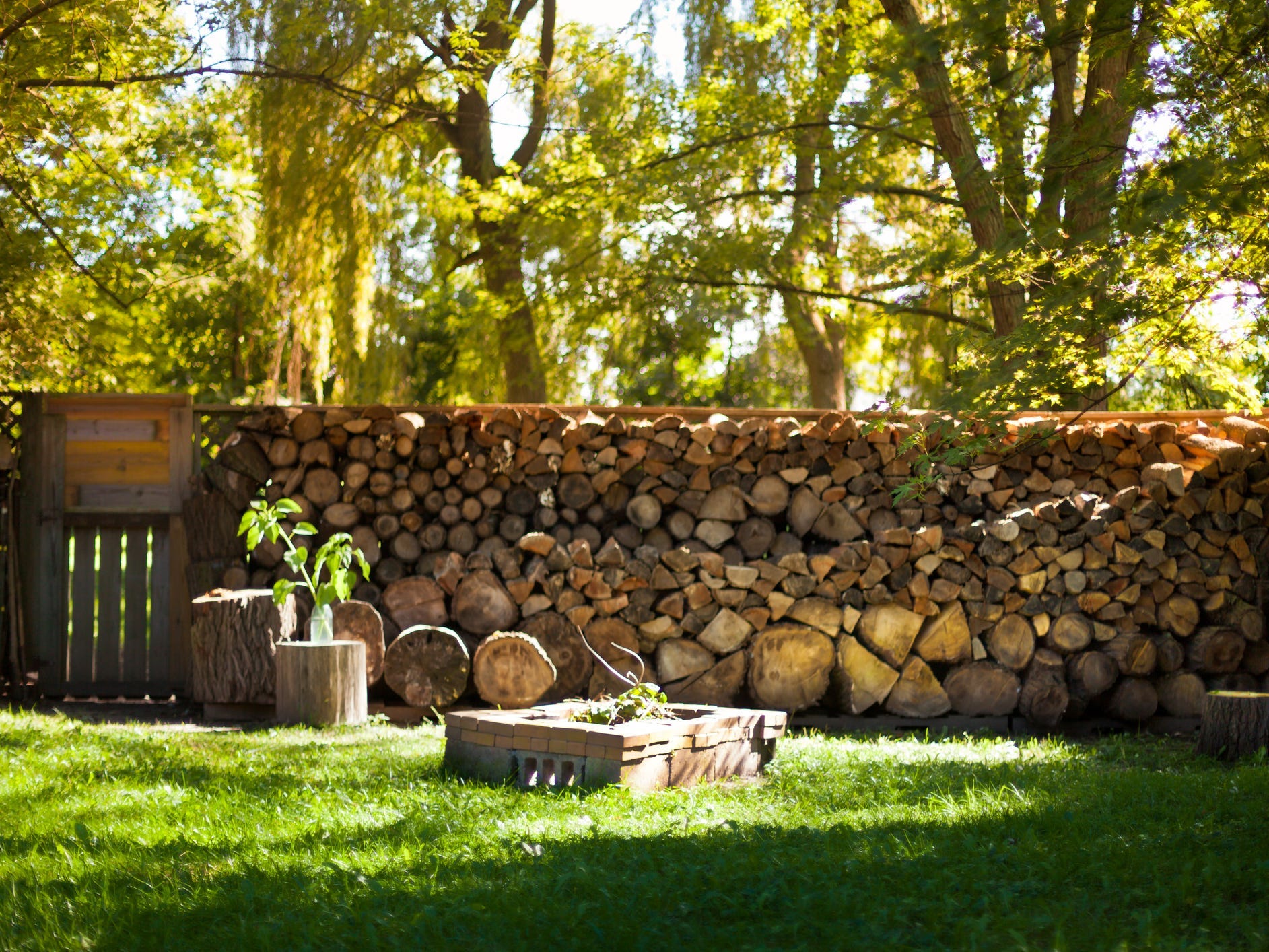 A large stack of firewood serving as the back wall to a fire pit area