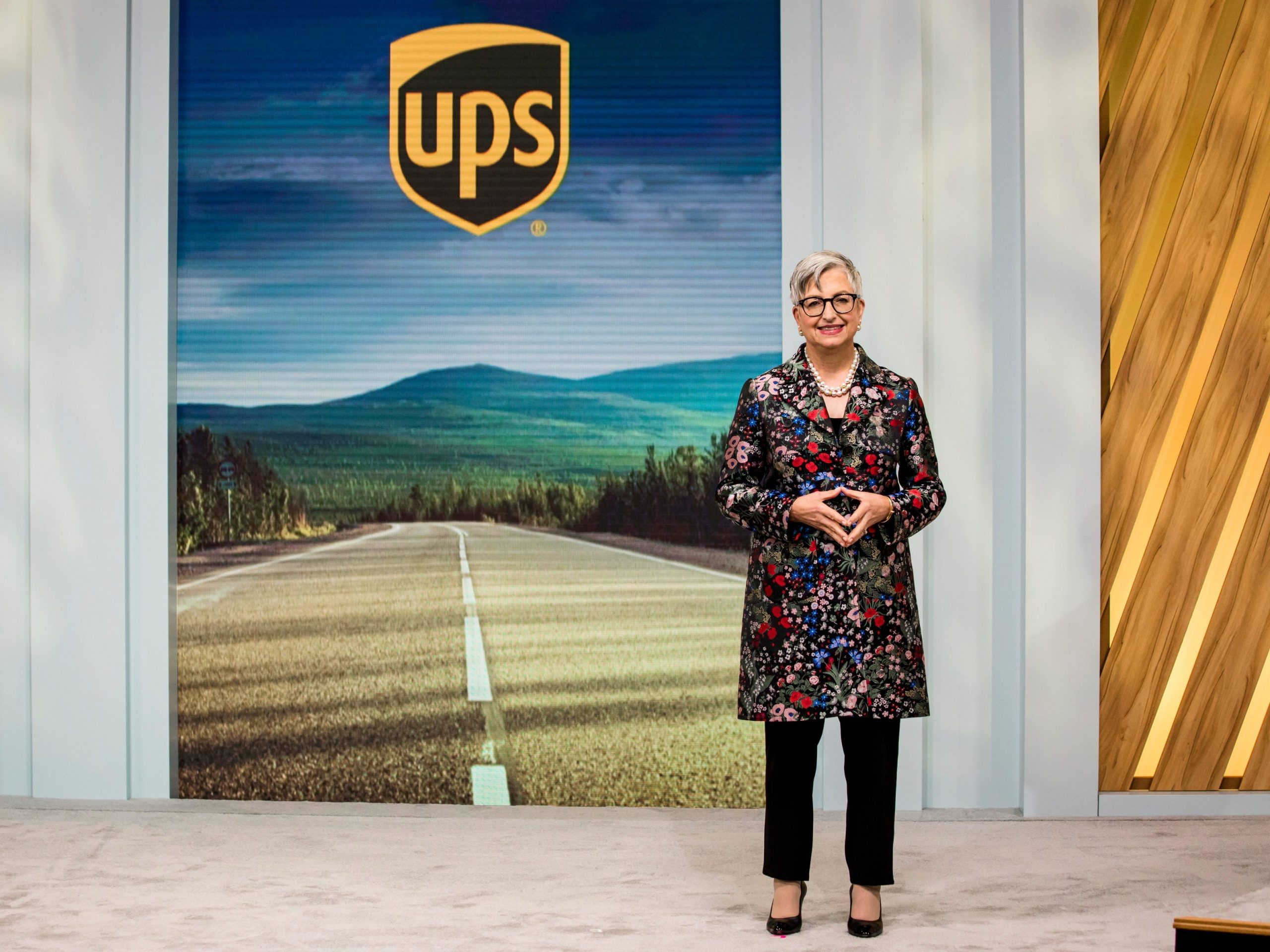 UPS CEO Carol Tomé presents on a stage before a UPS banner.