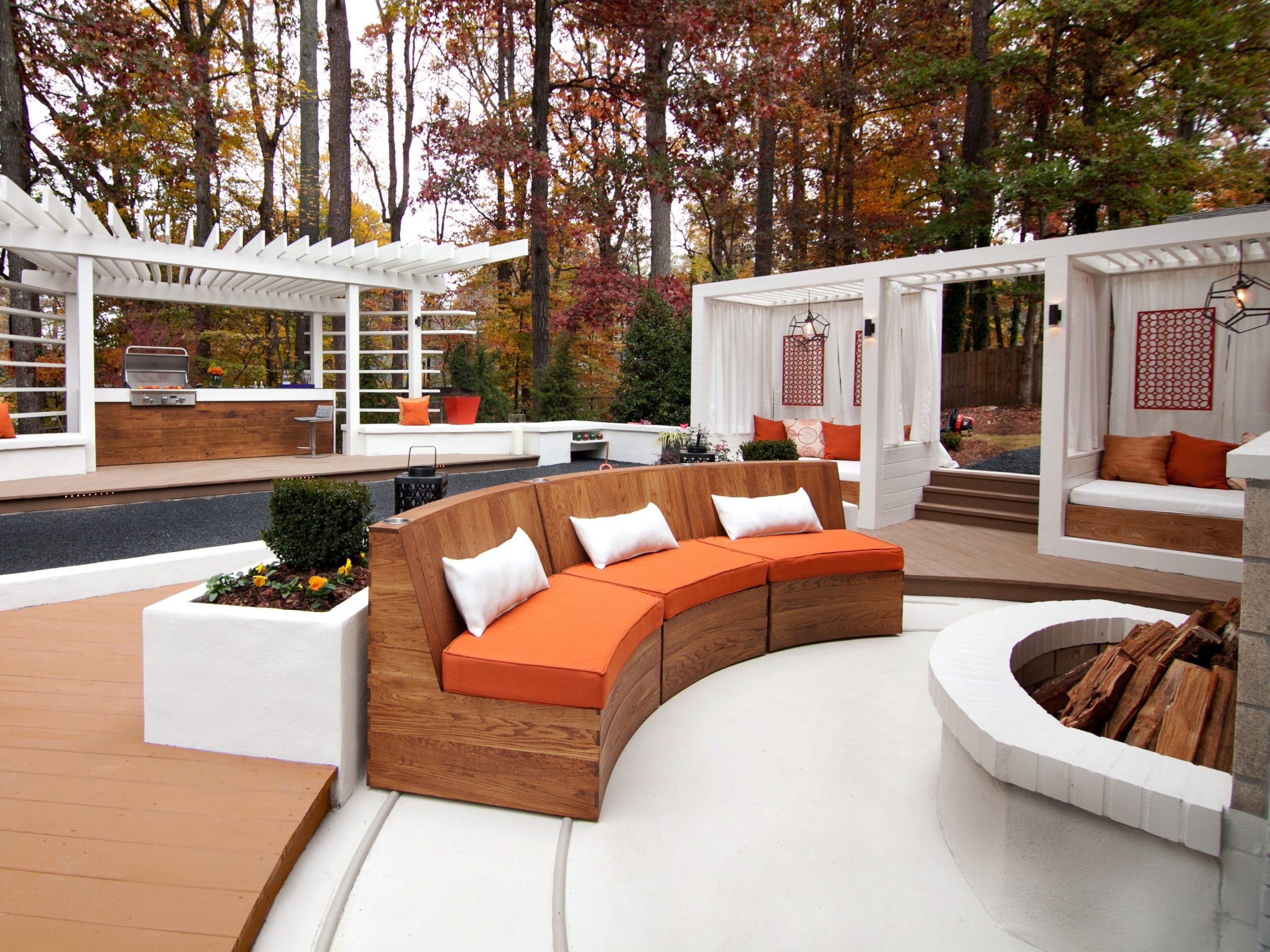 A luxury backyard with a grill, wooden decking, and a large couch in front of a fire pit