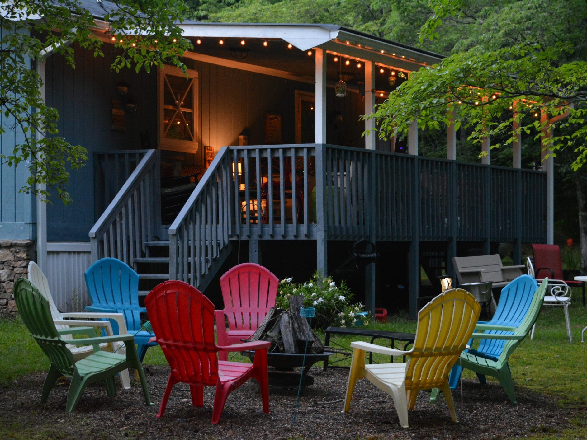 The backyard of blue cottage with a fire pit surrounded by colorful Adirondack chairs