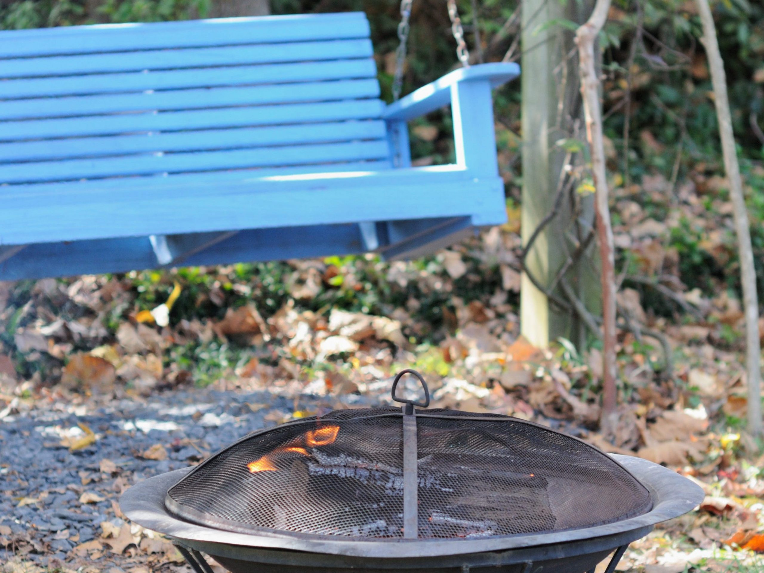A backyard fire pit with a blue bench swing in the background