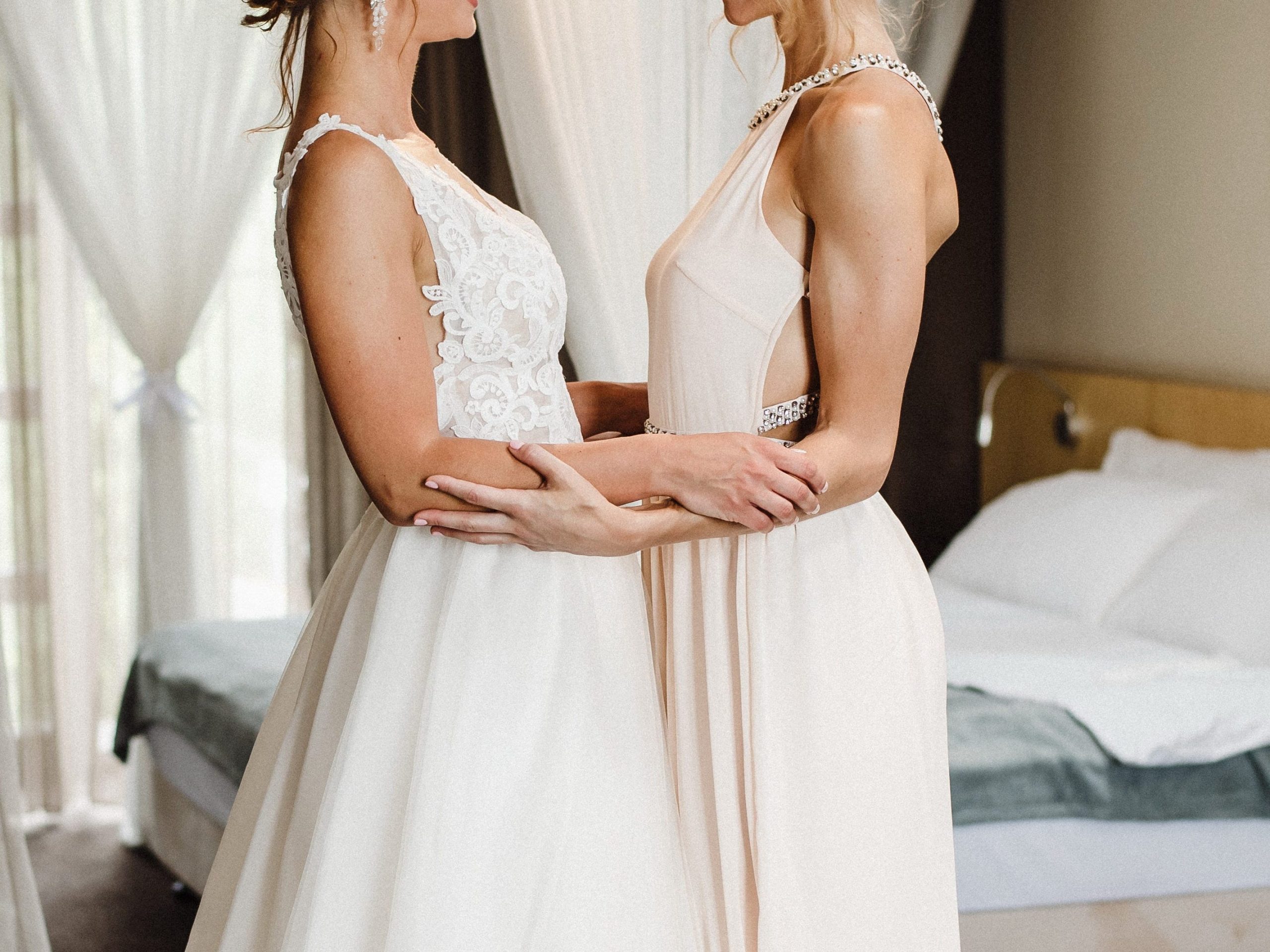 Two brides in white dresses looking at each other.