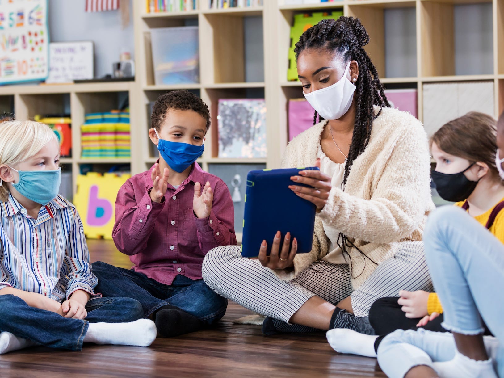 Teacher and students sitting together in a circle on the floor and wearing masks