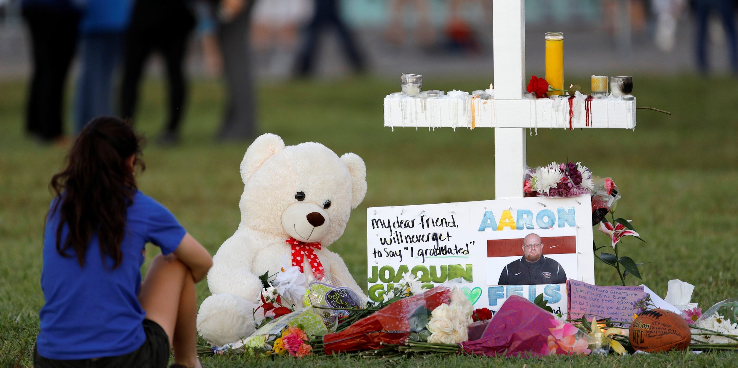 A mourner sits by a cross adorned with pictures of victims, along with flowers and other mementoes, at a memorial two days after the shooting at Marjory Stoneman Douglas High School in Parkland, Florida, U.S. February 16, 2018.