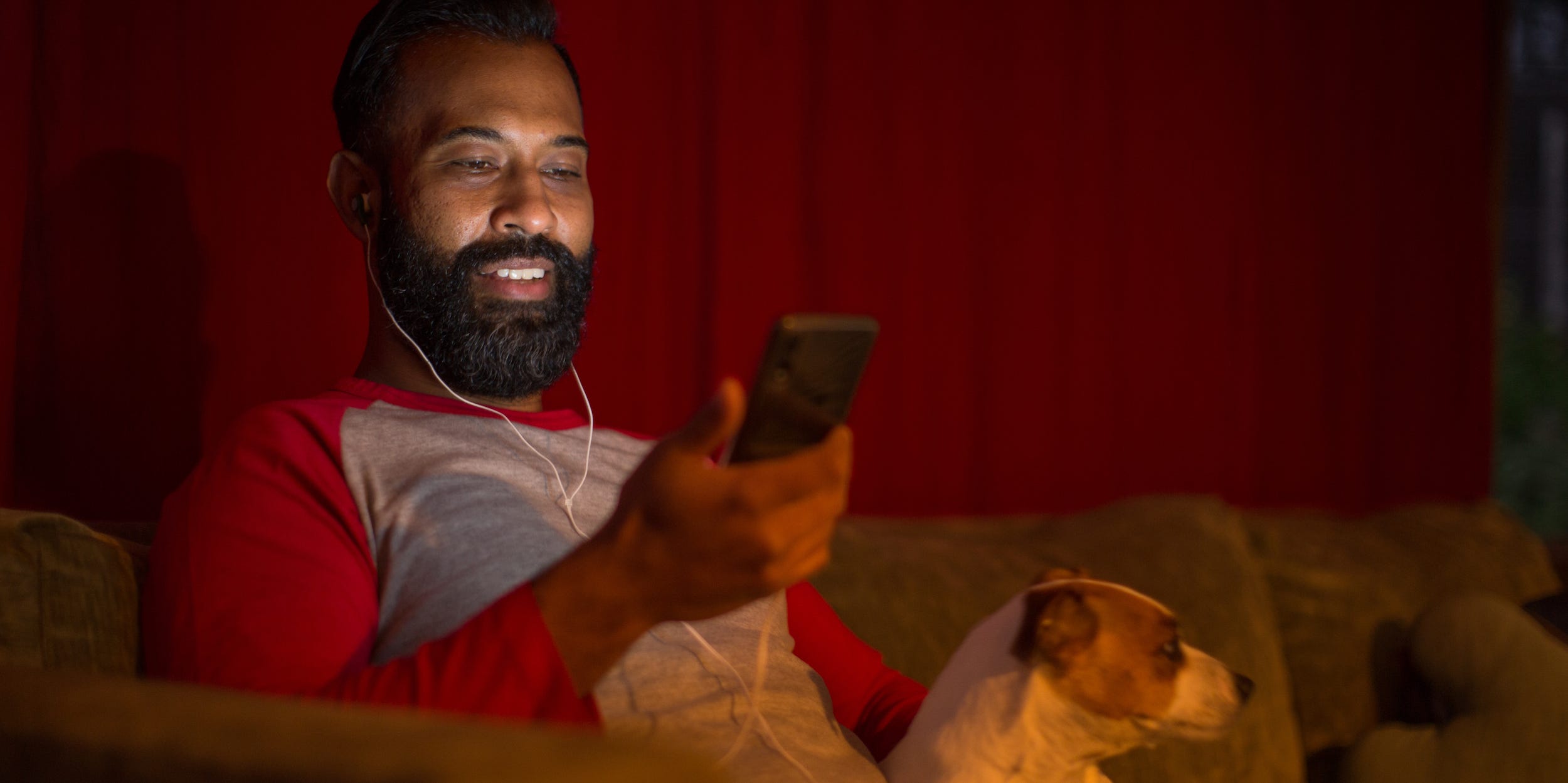 Man using smartphone with earbuds at home on couch