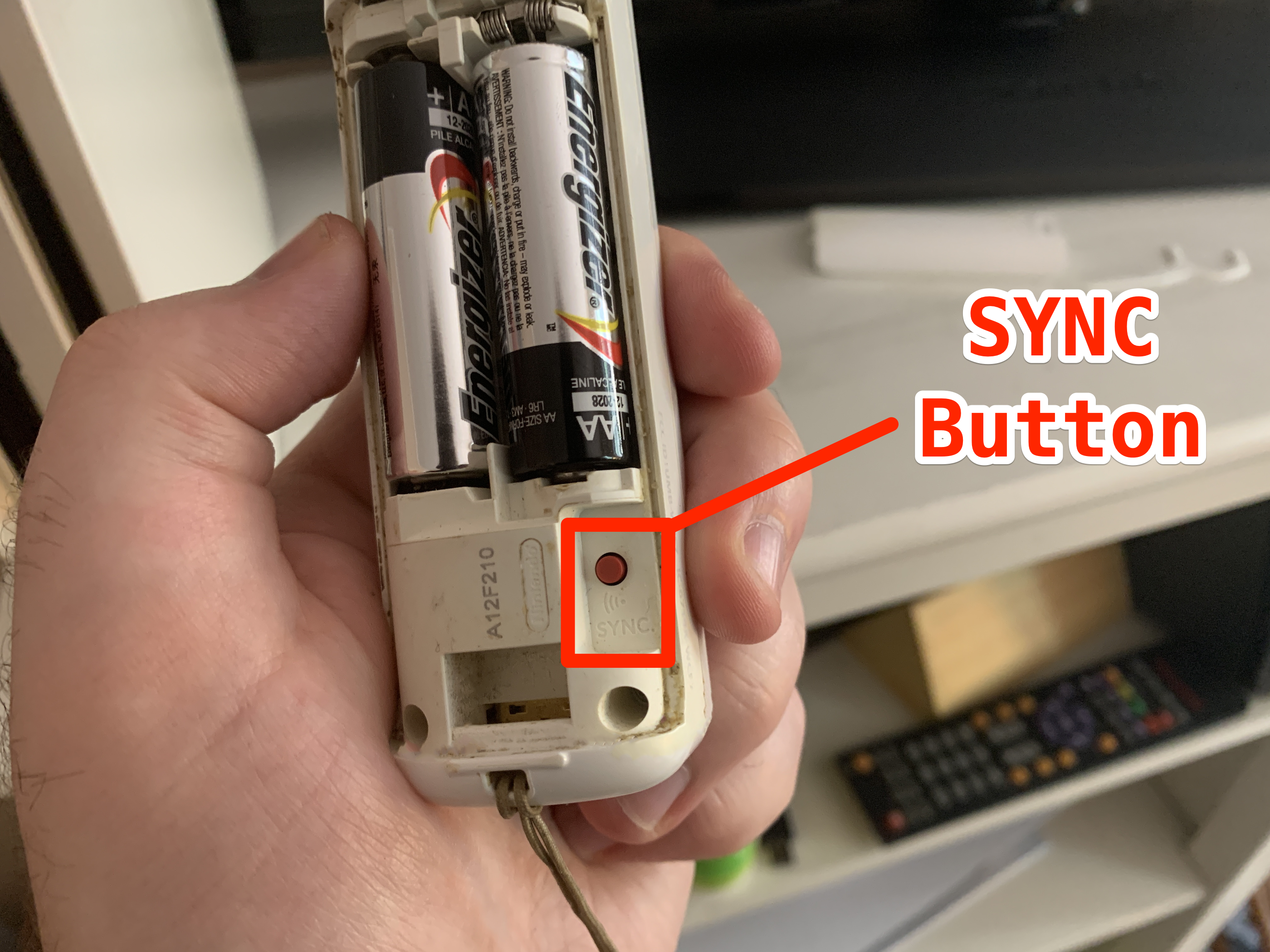 A Wii Remote with the battery cover removed and the SYNC button highlighted.