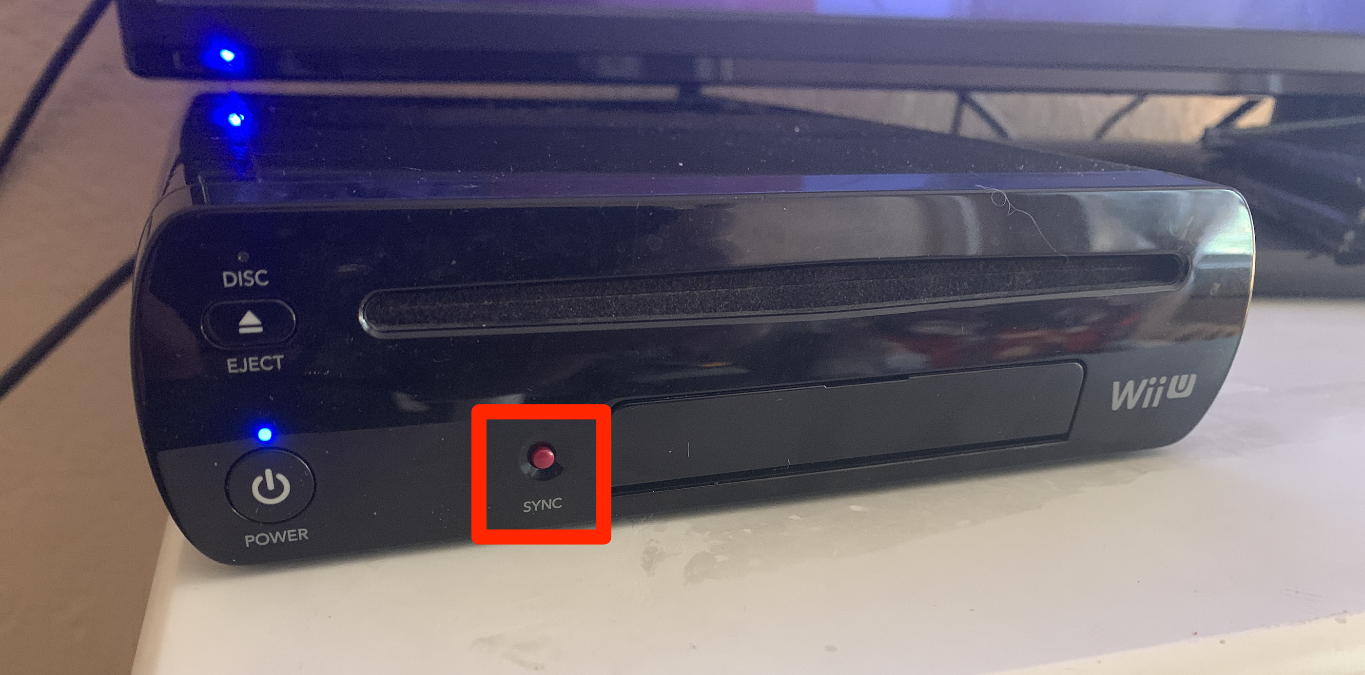 A Wii U console. Its SYNC button is highlighted.