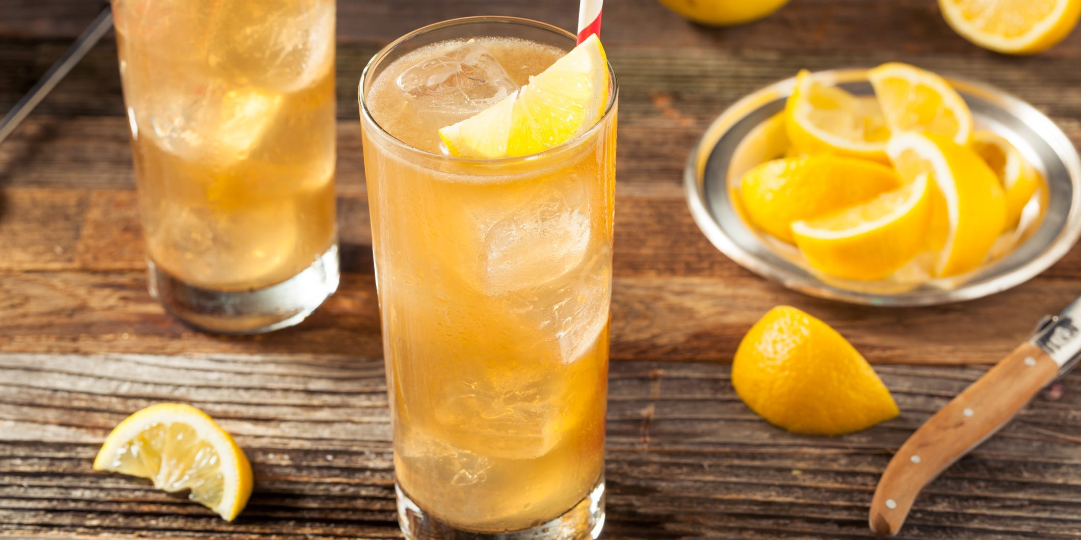 Two Long Island iced tea cocktails garnished with lemon, next to a silver plate of lemon slices