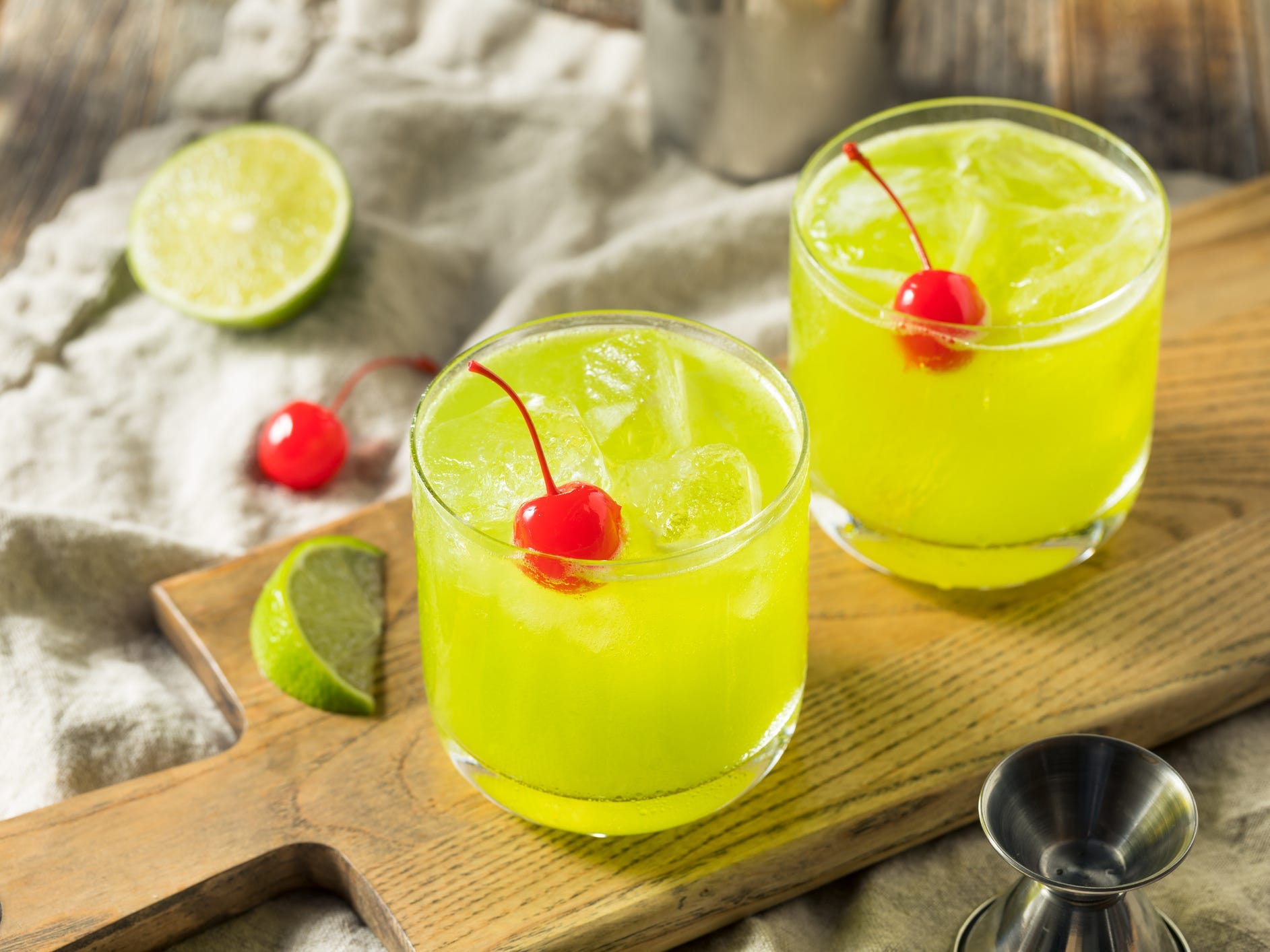 Two glasses of a bright green midori cocktail topped with maraschino cherries