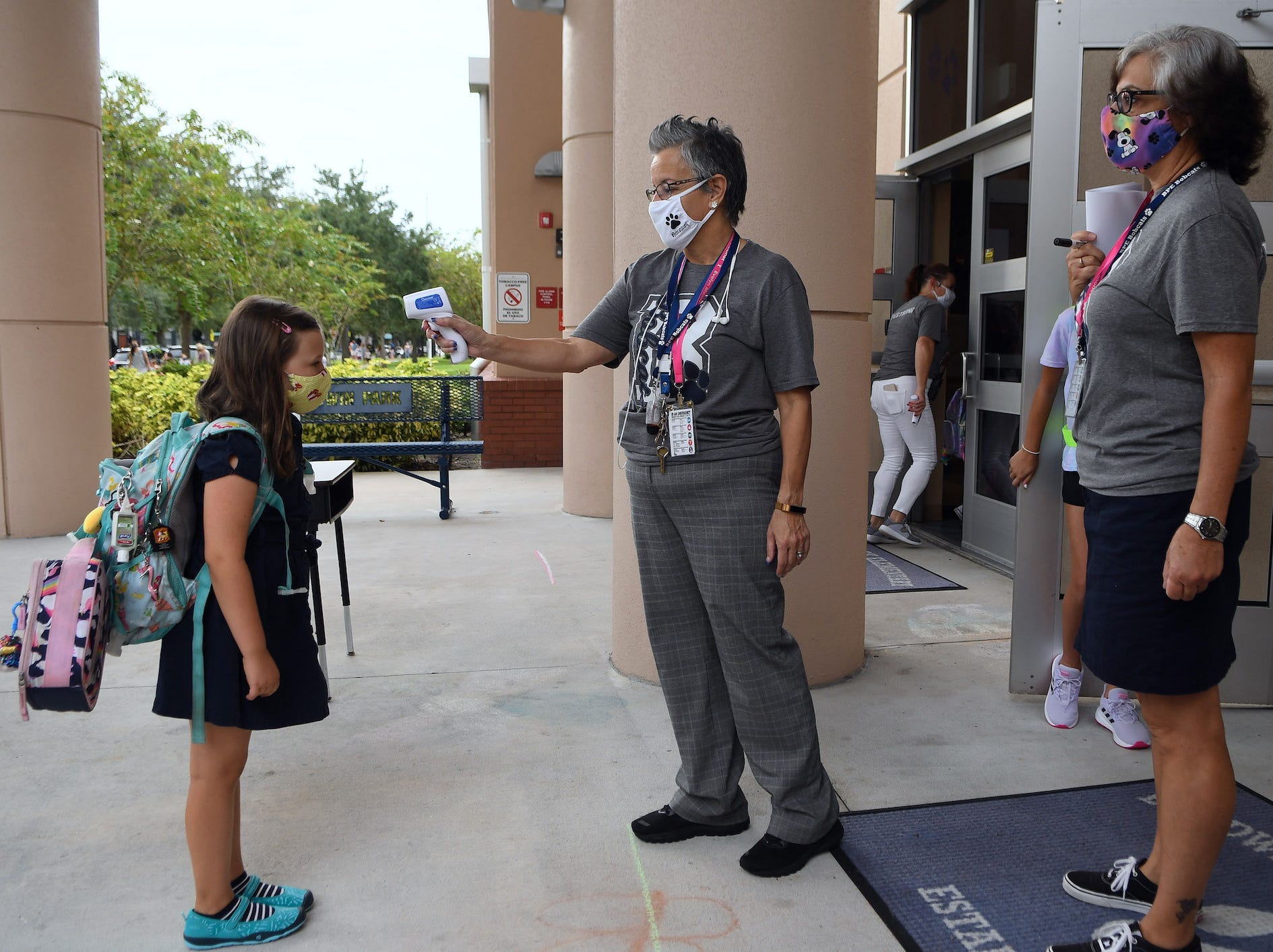 A schoolteacher, wearing a mask, checks the temperature of one of her masked students, before the child is let inside.