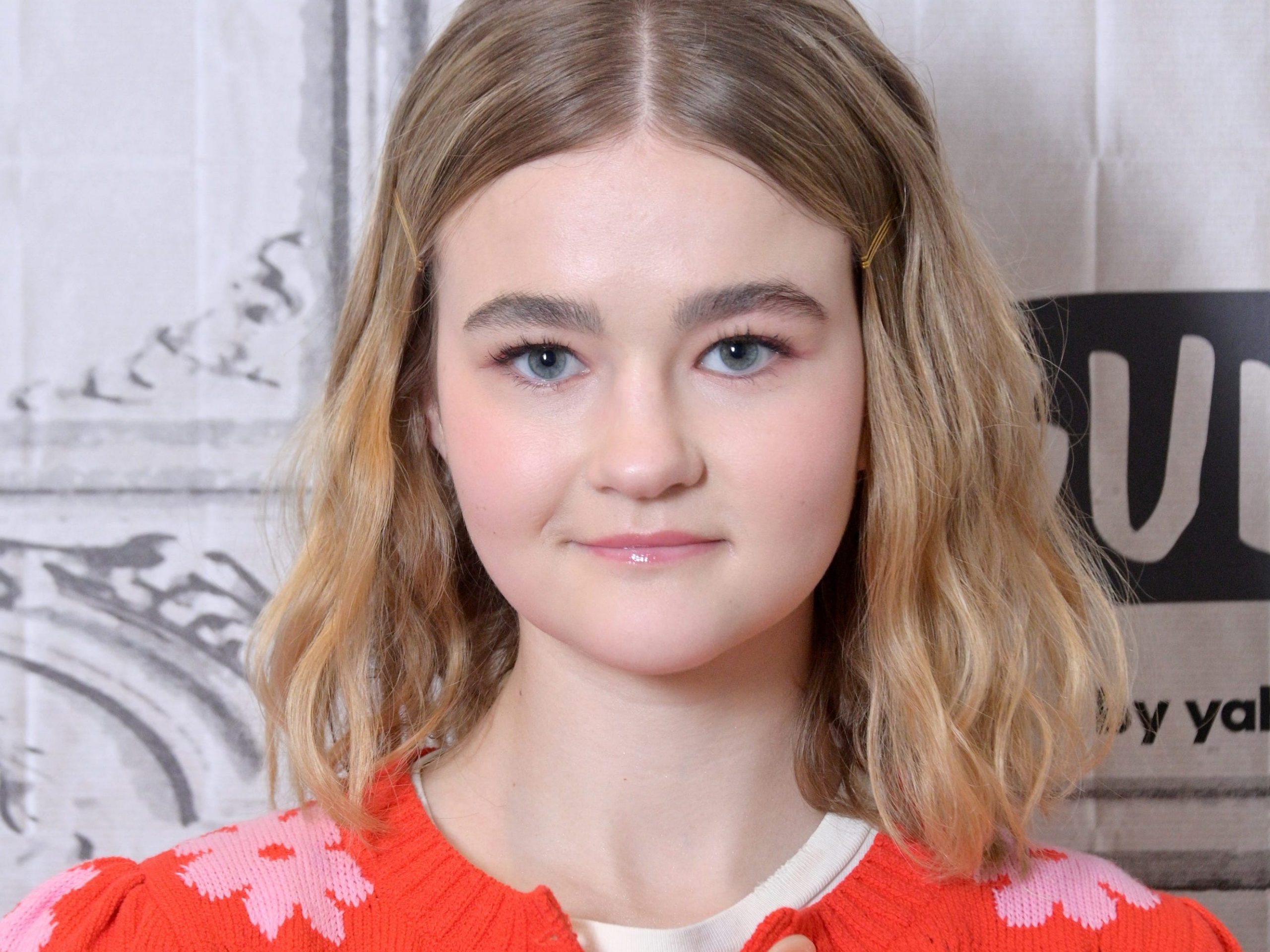Millicent Simmonds in an orange cardigan with pink flowers.