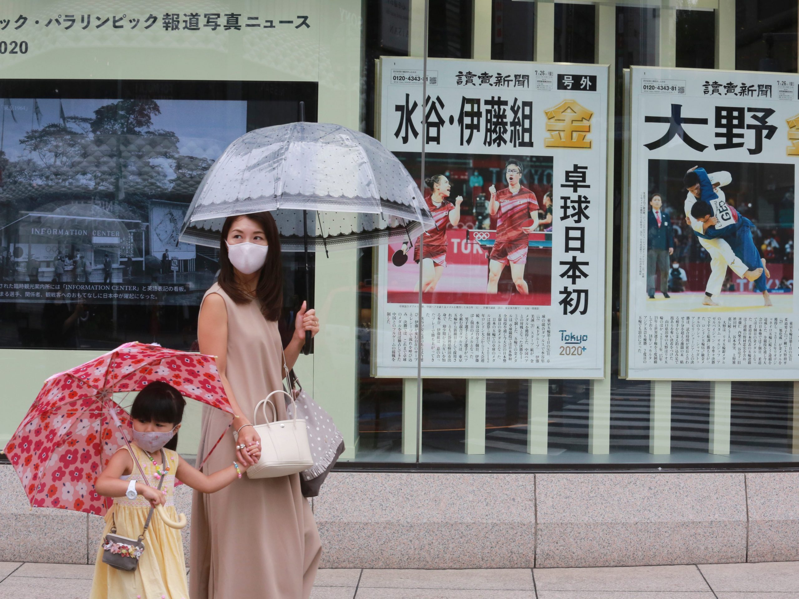 People wearing face masks to protect against the spread of the coronavirus walk past extra papers reporting on Japanese gold medalists at Tokyo Olympics, in Tokyo Tuesday, July 27, 2021.